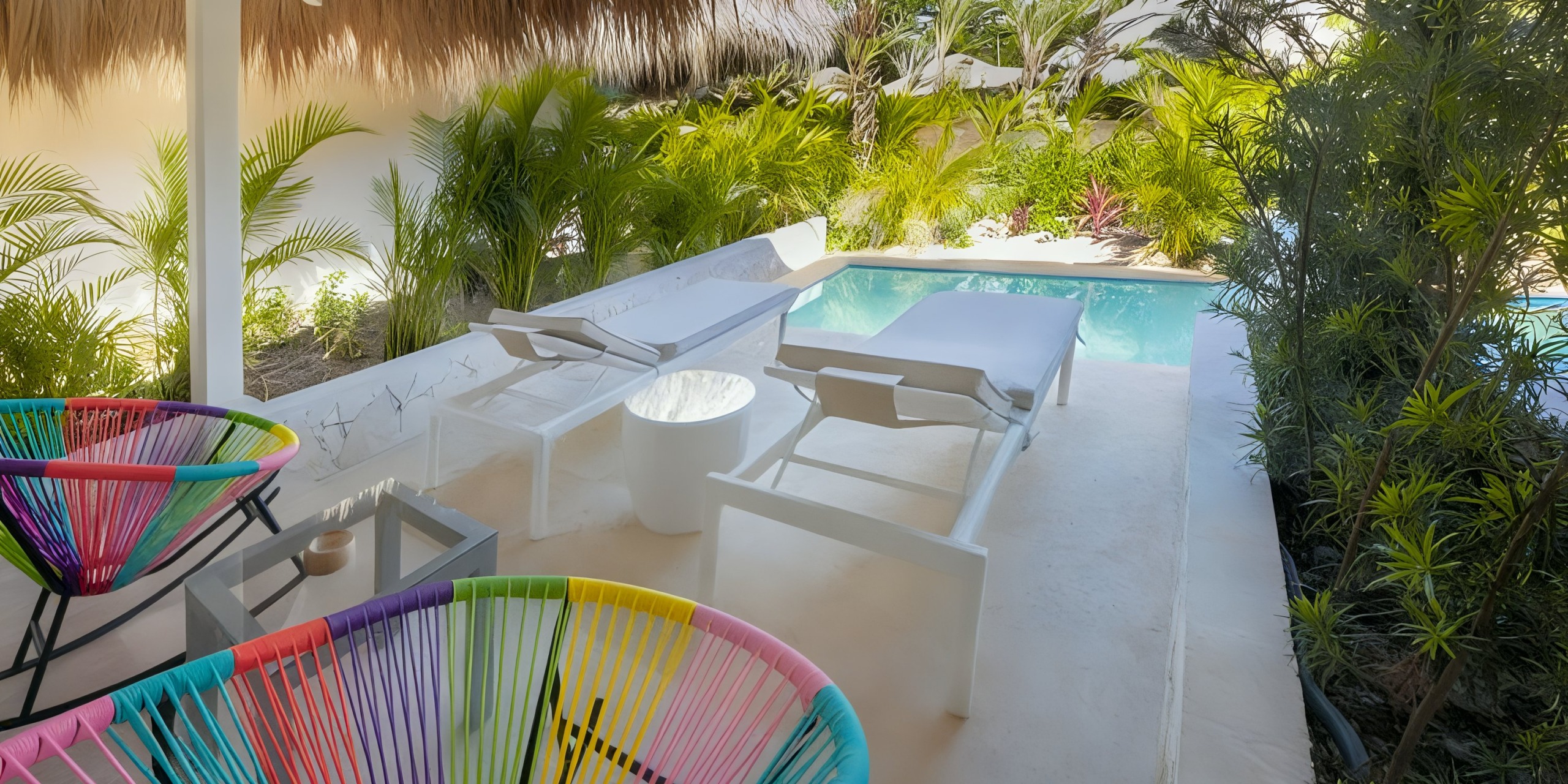 Experience the tropical outdoor patio at Viva V Samana by Wyndham, featuring white loungers, colorful chairs, a small pool, and lush greenery all around.