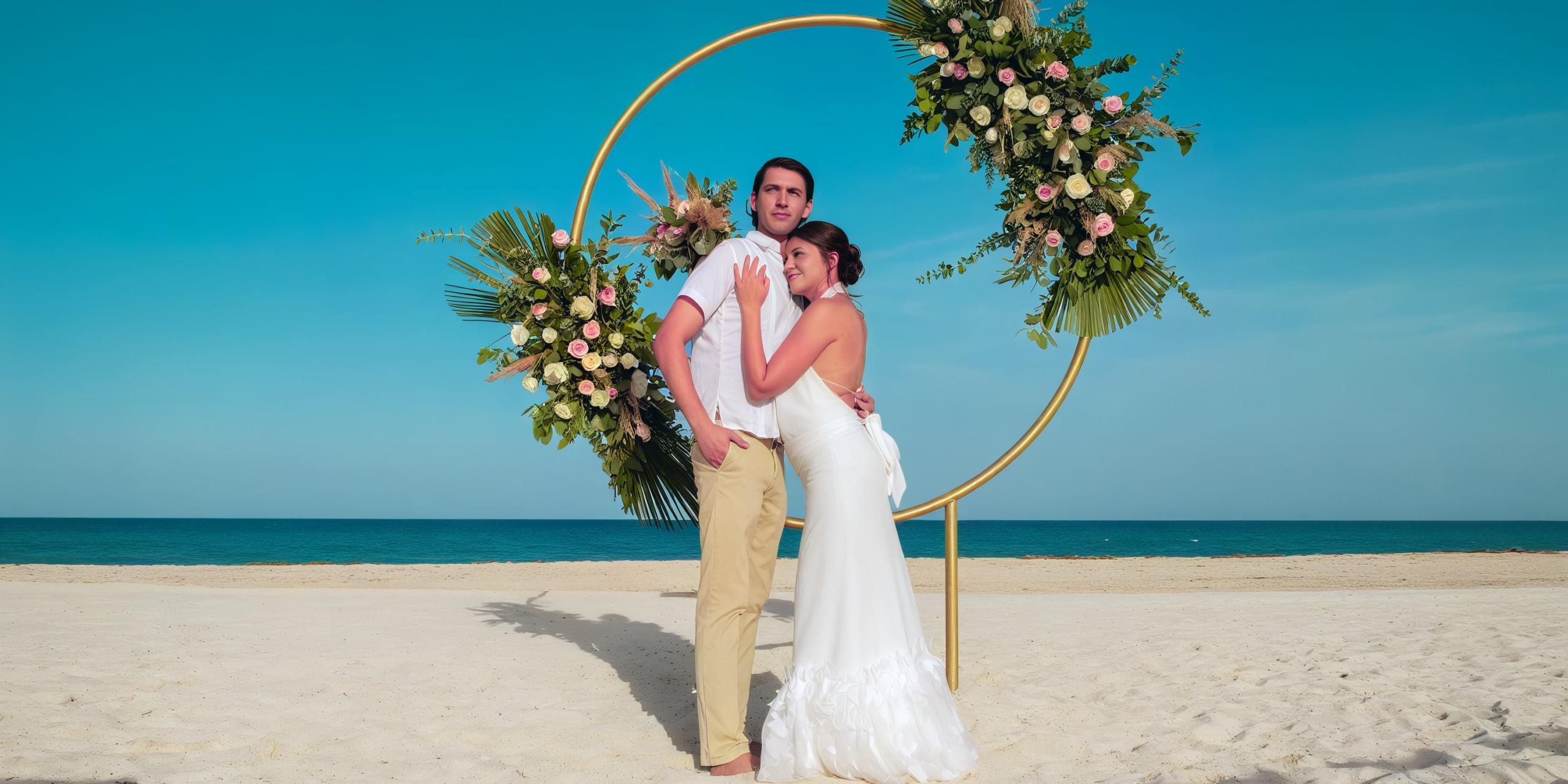 A couple stands on a sandy beach in front of a circular floral arch at the Wyndham Grand Cancun.
