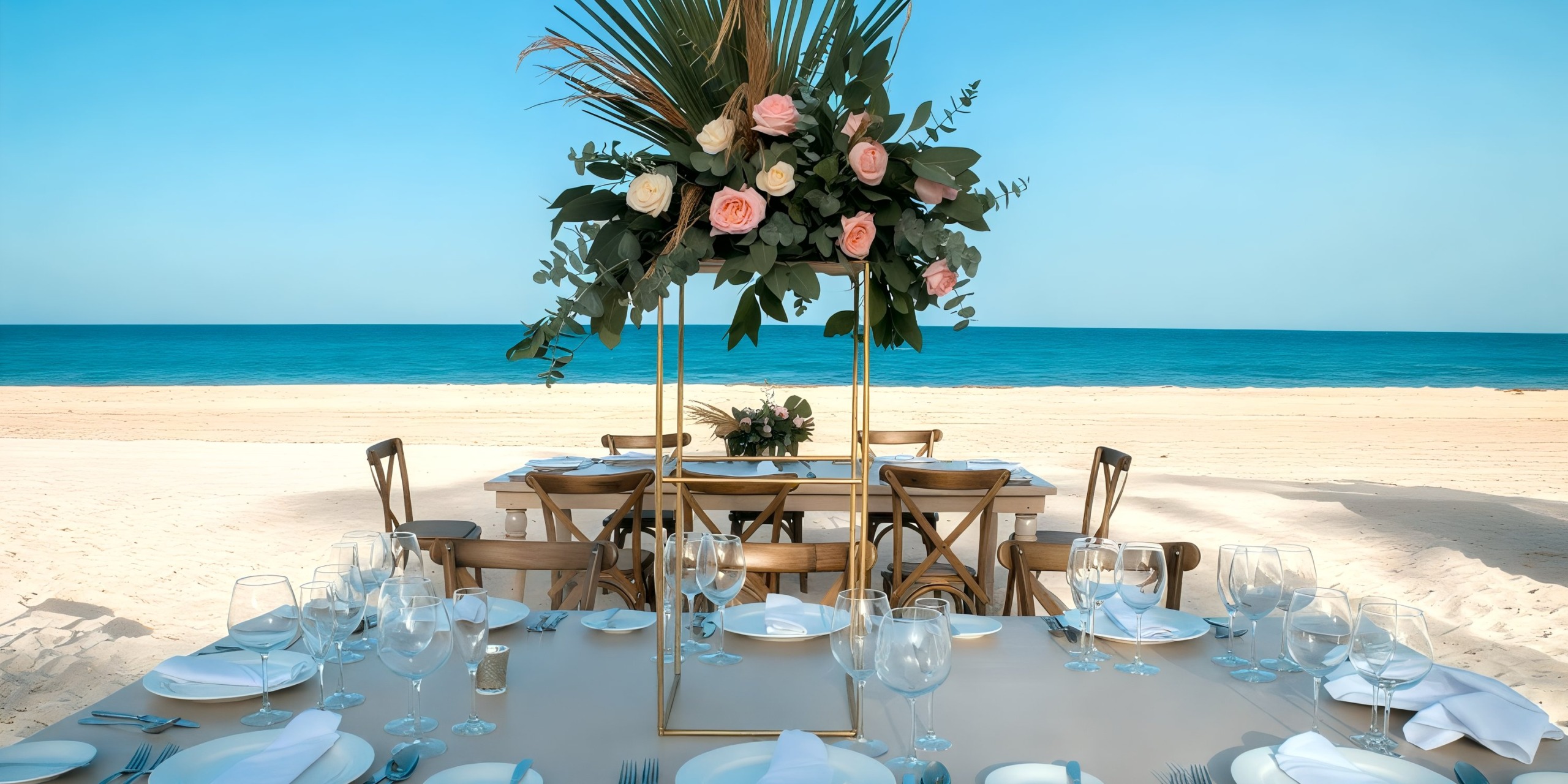 Table set for a meal at Wyndham Grand Cancun, featuring a floral centerpiece and surrounded by wooden chairs, with the ocean and clear sky in the background.