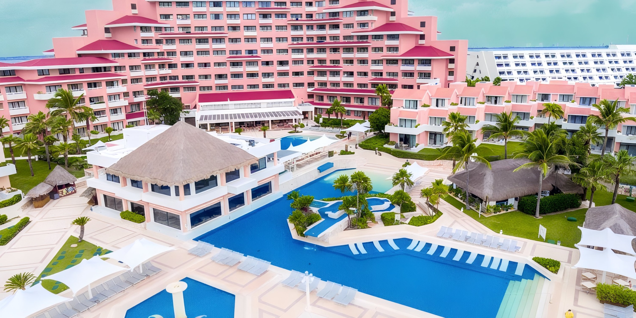 Aerial view of the Wyndham Grand Cancun, a sprawling pink resort featuring numerous pools, sun loungers, and palm trees.