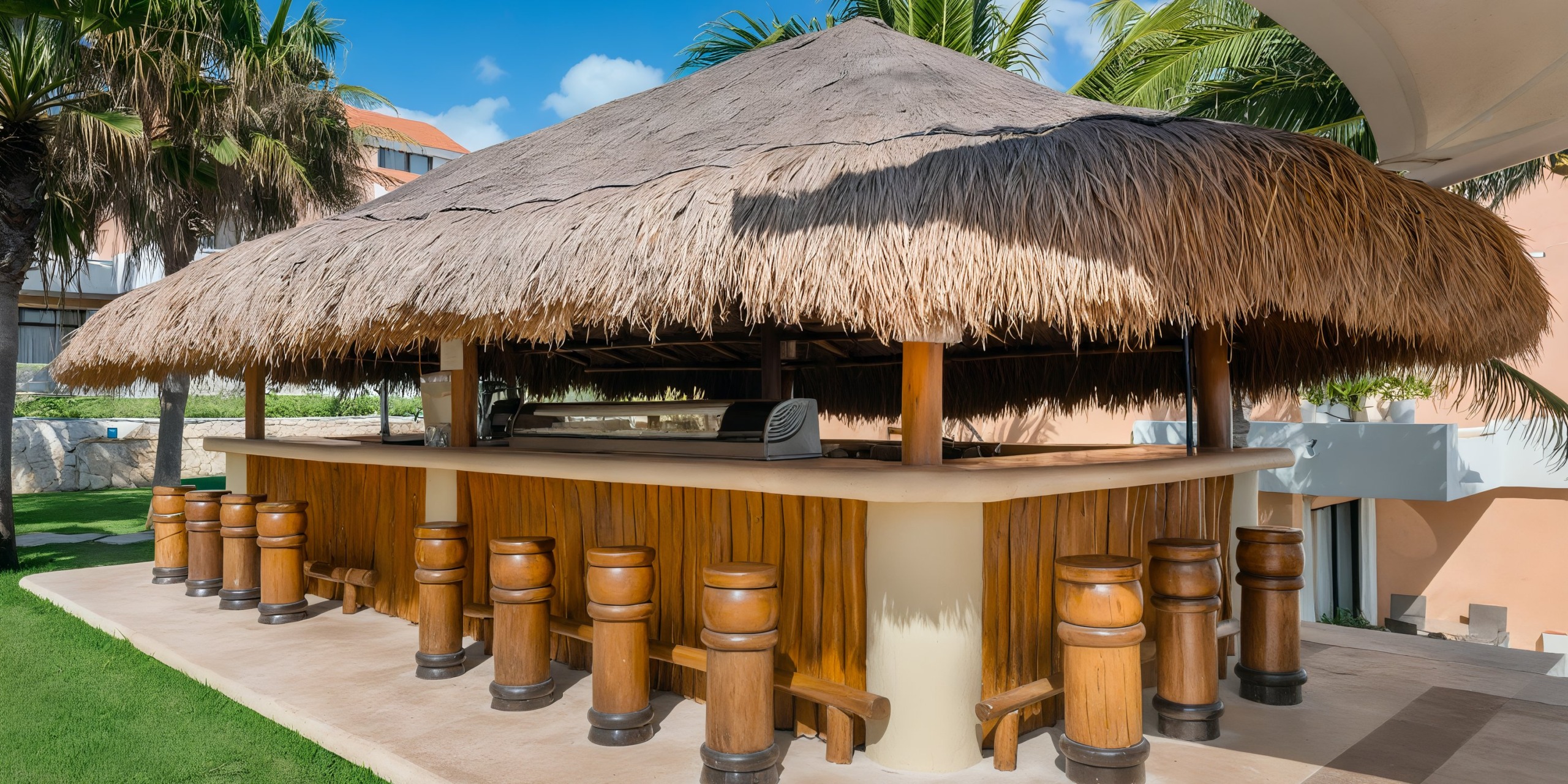 Wyndham Grand Cancun features an outdoor tiki bar with a thatched roof, surrounded by wooden stools, all set in a tropical environment with palm trees and clear skies.