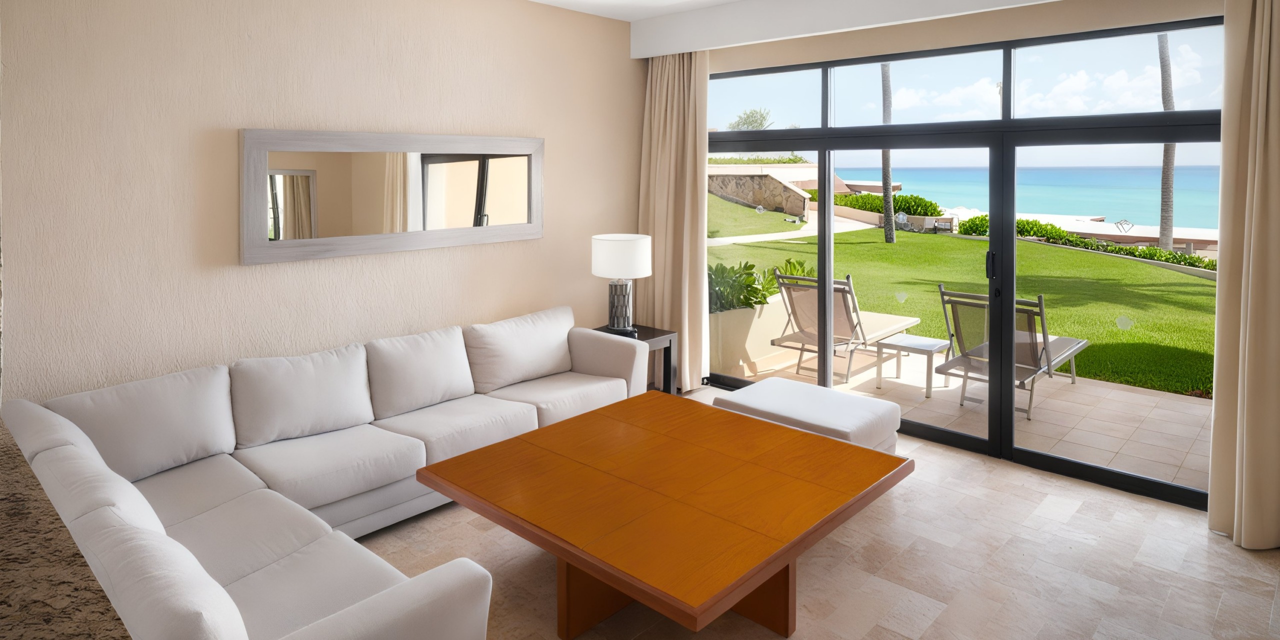 A spacious living room at Wyndham Grand Cancun features a white sectional sofa, a wooden coffee table, and a floor lamp. Large windows open to a patio equipped with chairs and offer a serene view of the grass and ocean.
