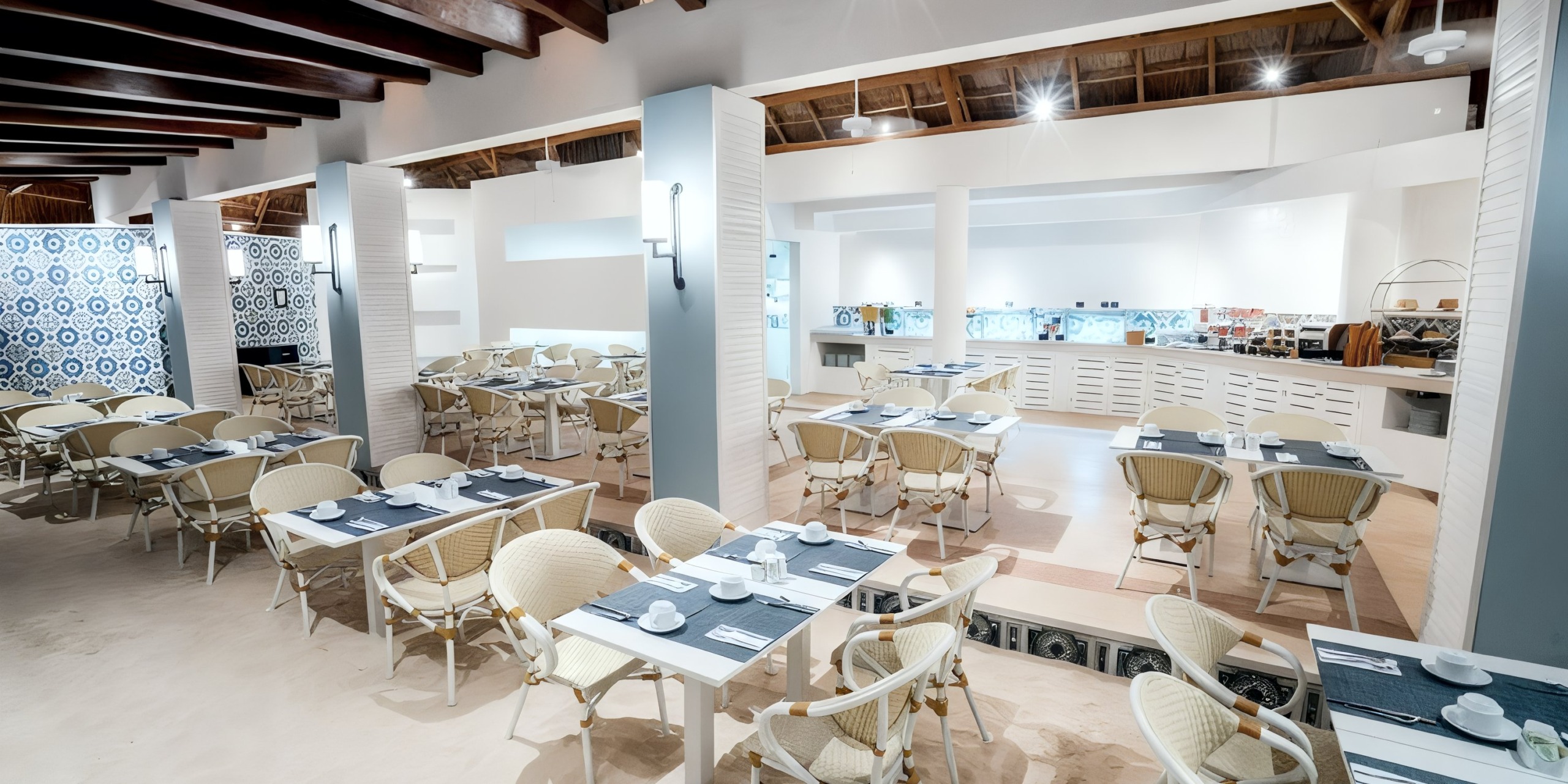 The interior of the Wyndham Grand Cancun features a modern design with white and beige decor, complemented by wicker chairs and tables set elegantly with place settings.