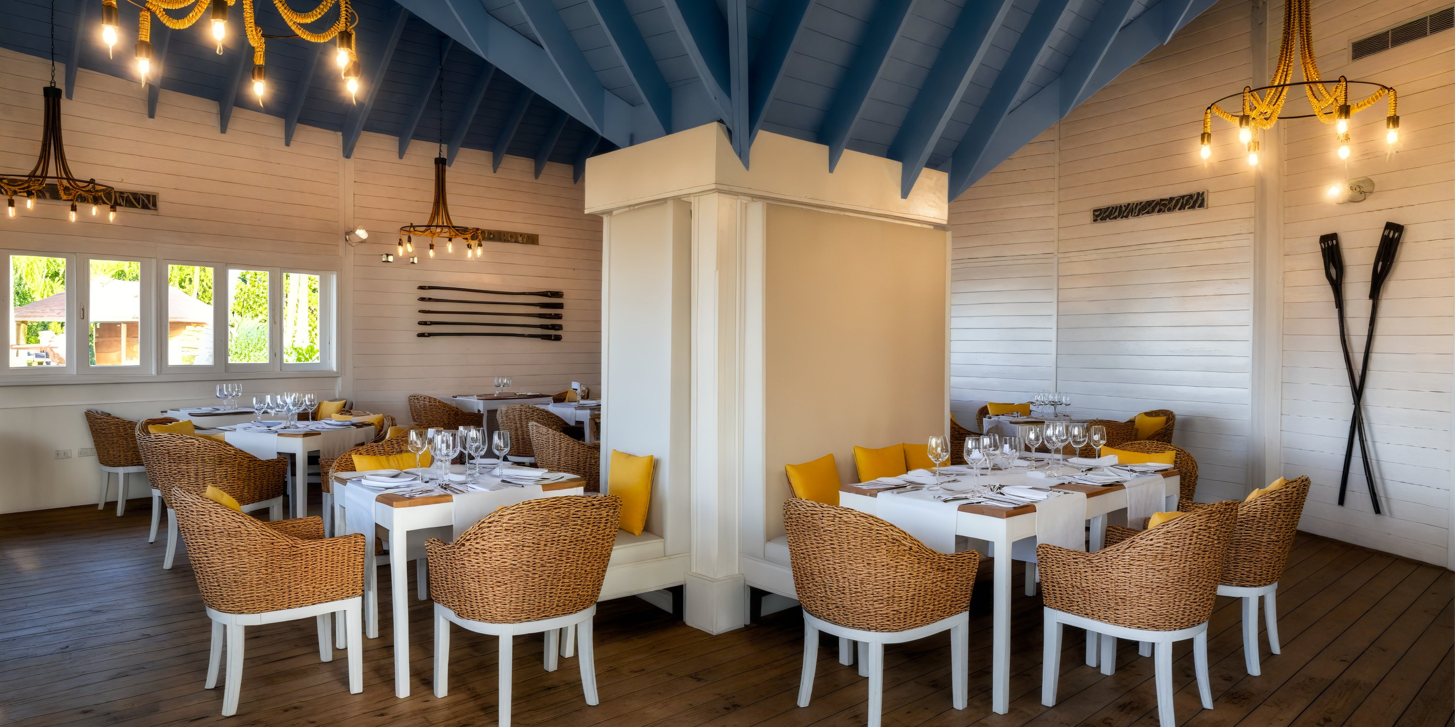 The restaurant boasts a cozy interior, perfect for a destination wedding, featuring wicker chairs, elegant white tables, and a stunning blue ceiling.