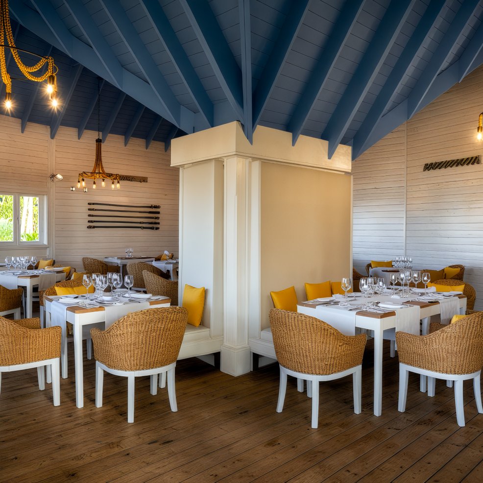 The interior of the restaurant, ideal for a destination wedding, features charming wicker chairs and a ceiling adorned with blue wooden beams.