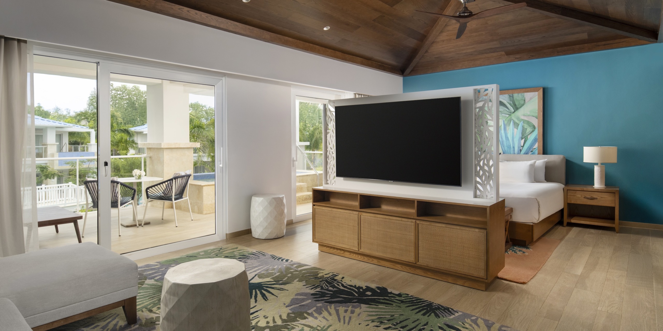 Experience the Dreams Cap Cana Resort & Spa with a cozy king-sized bed, large TV, and seating area. Enjoy your private balcony with patio furniture via a sliding glass door. The room features light wood accents and includes a ceiling fan for added comfort.