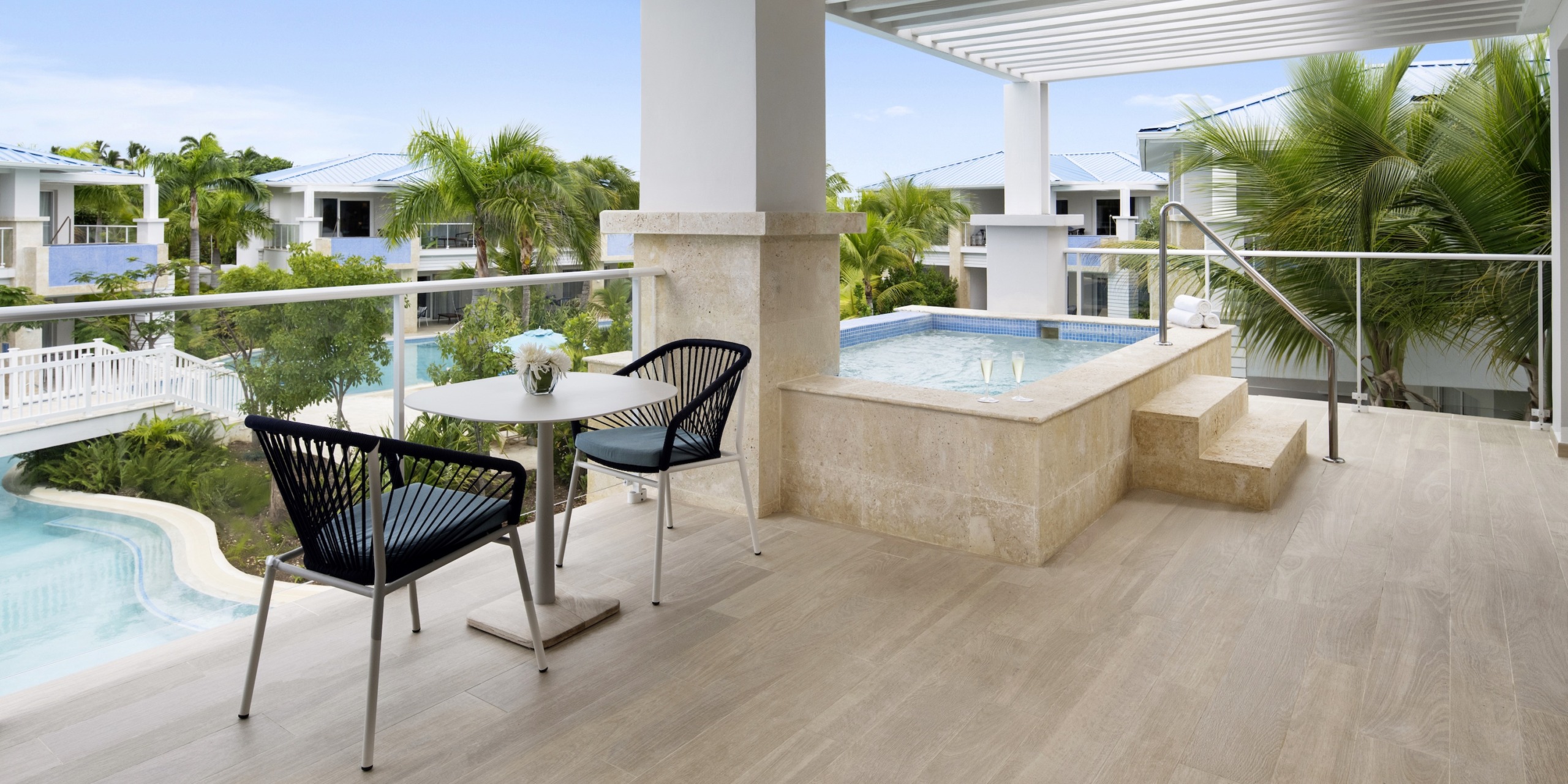 The Dreams Cap Cana Resort & Spa features an outdoor terrace with a table, two chairs, and a small pool, surrounded by lush tropical greenery and modern white buildings.