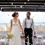 A bride and groom hold hands, smiling as they walk down an outdoor aisle adorned with scattered flower petals.