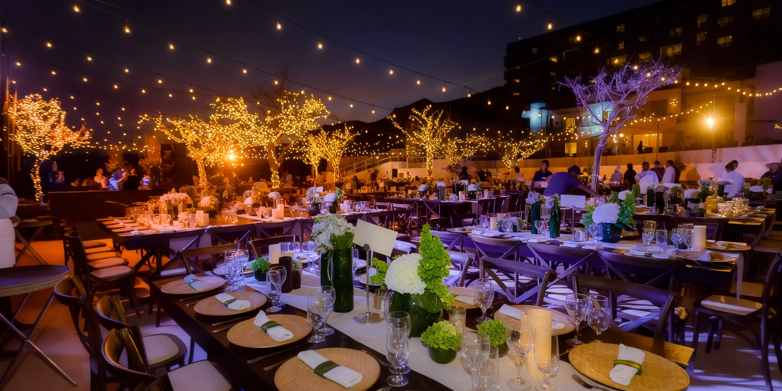 A festive evening event at Marquis Los Cabos features tables set for dining, string lights overhead, illuminated trees, and people gathered in the background.