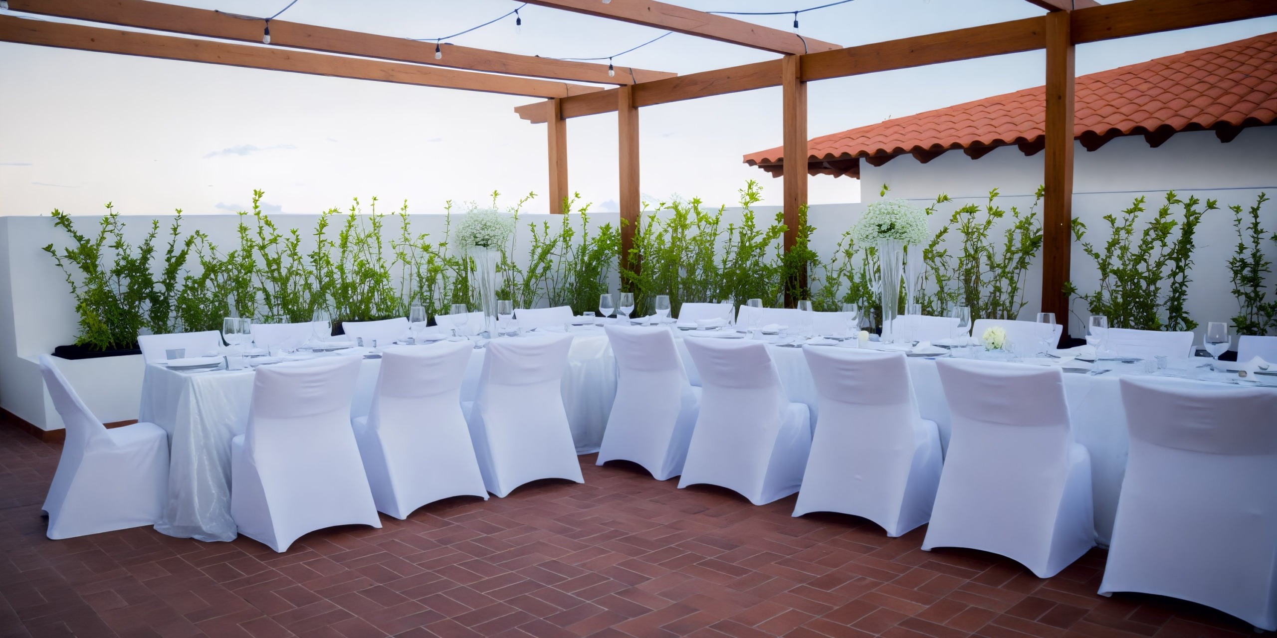 A picturesque outdoor dining area, perfect for a wedding, featuring white tablecloths and chairs elegantly arranged under a charming pergola.