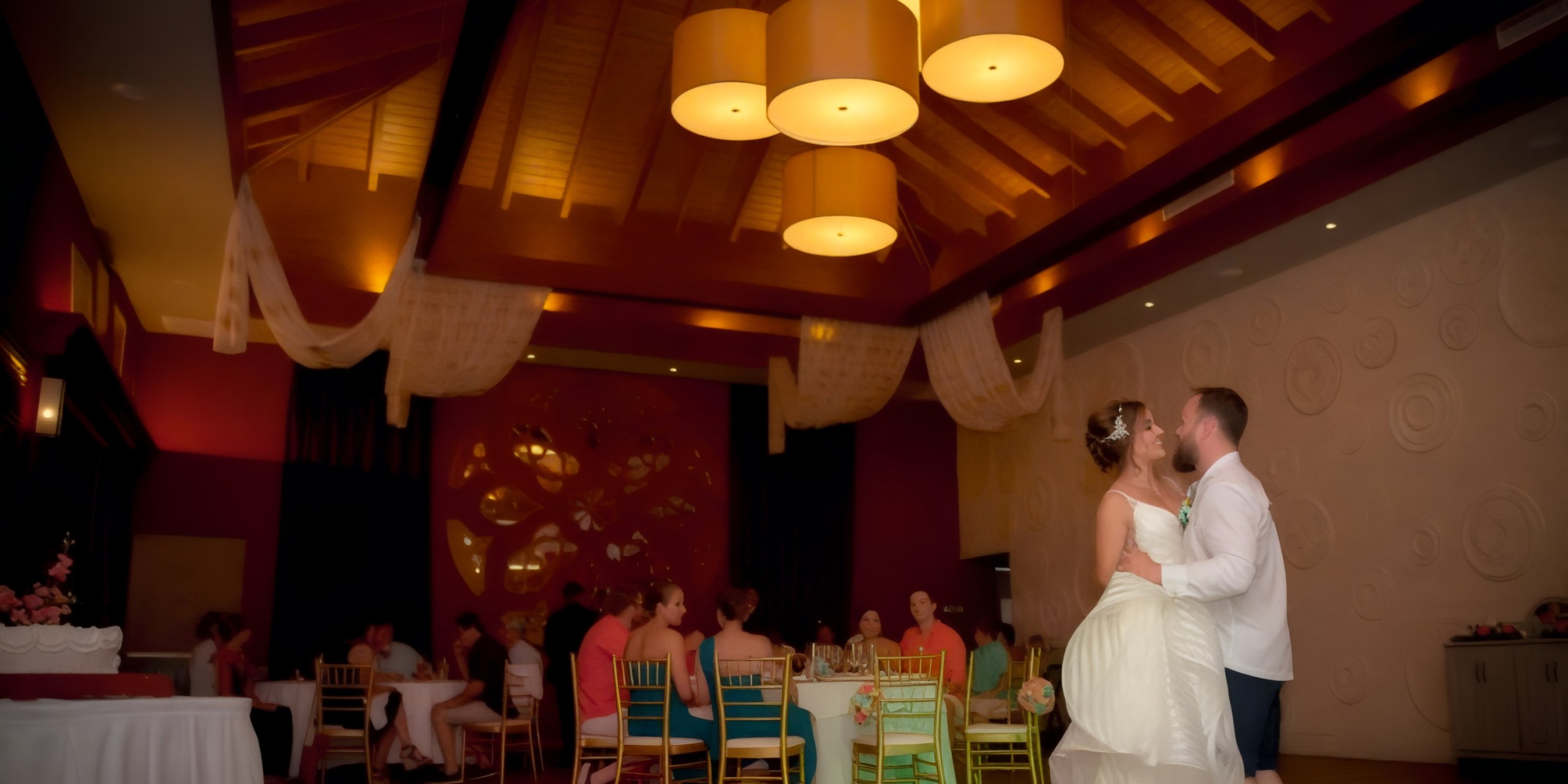 A couple dances in a warmly lit event hall during their destination wedding, with seated guests visible in the background.