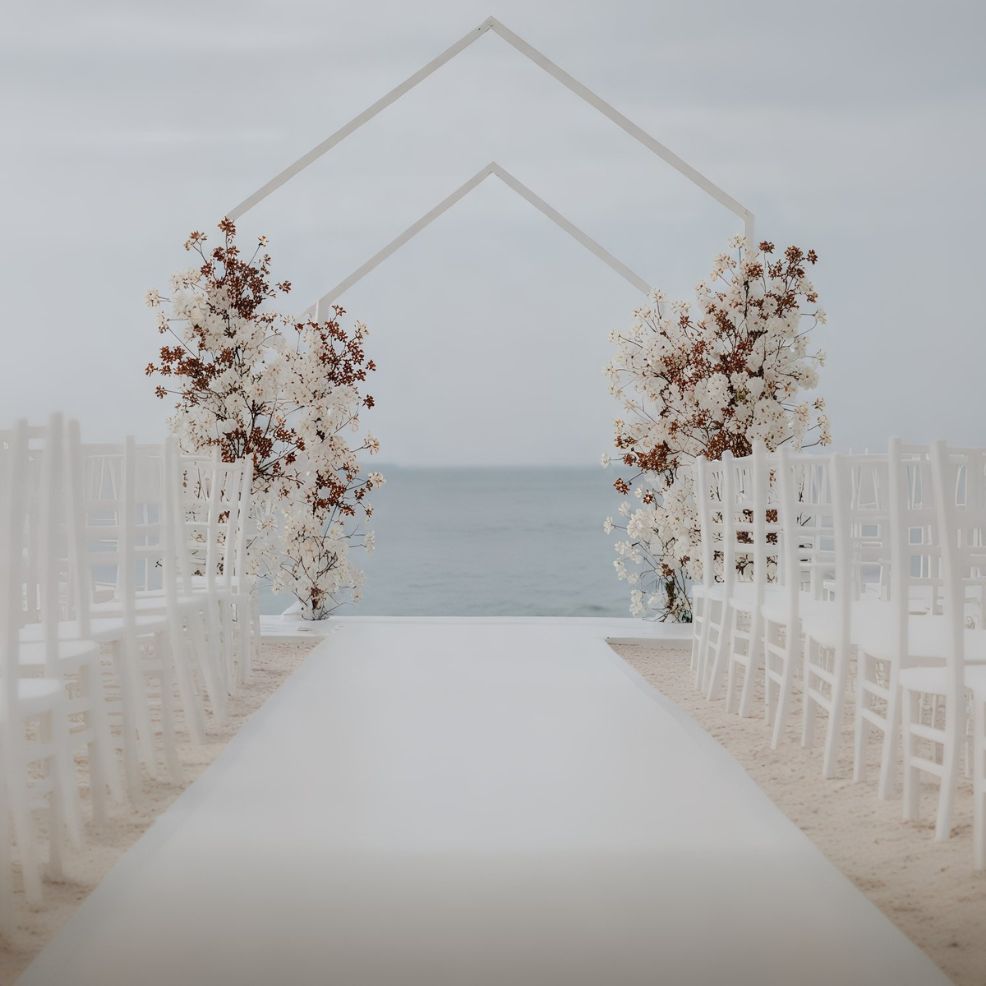 A picturesque destination wedding setup on the beachfront, featuring white chairs and a floral arch with stunning ocean views.