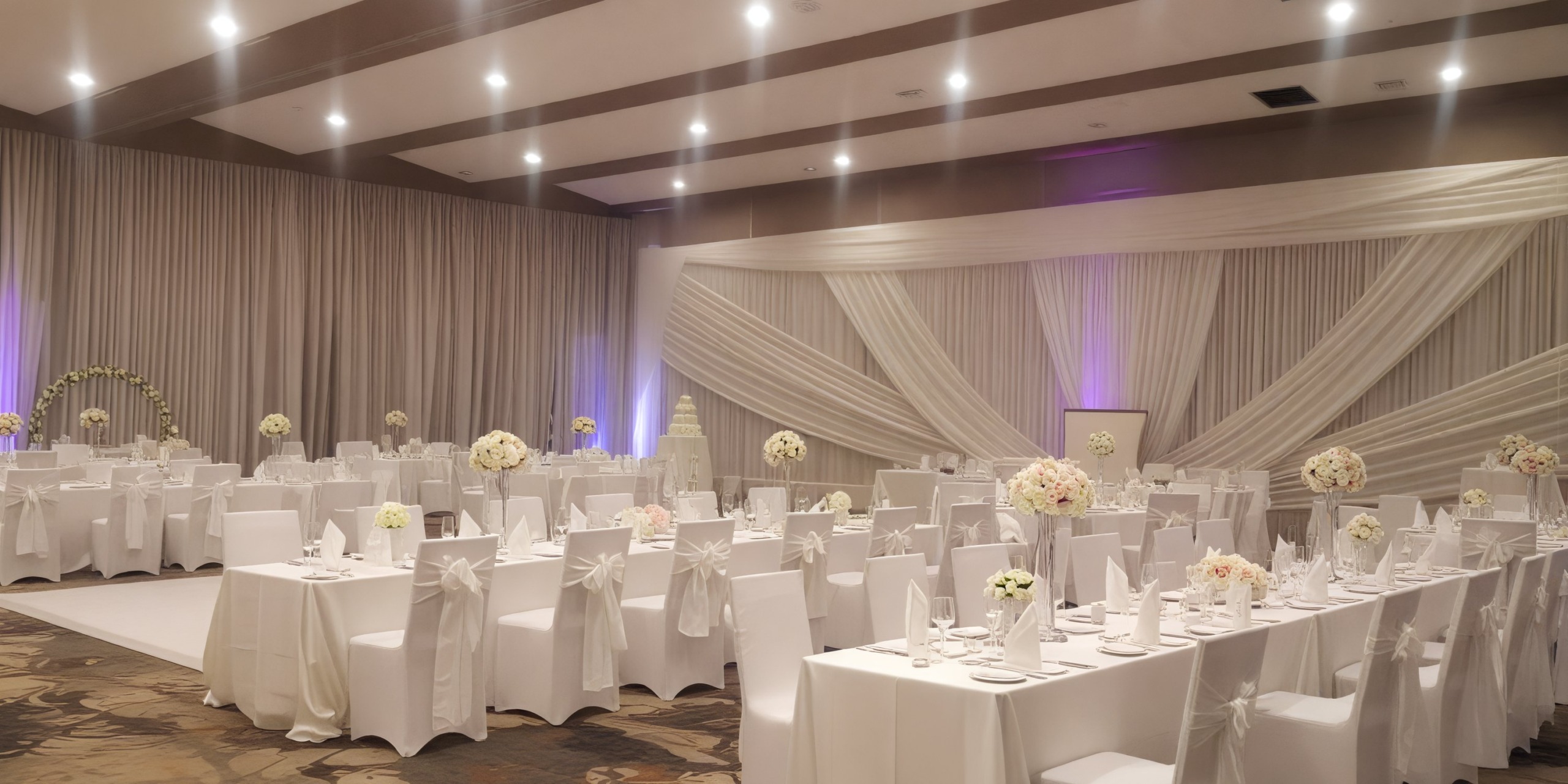 An elegant banquet hall adorned with white decor and floral centerpieces, perfect for a wedding or destination wedding.