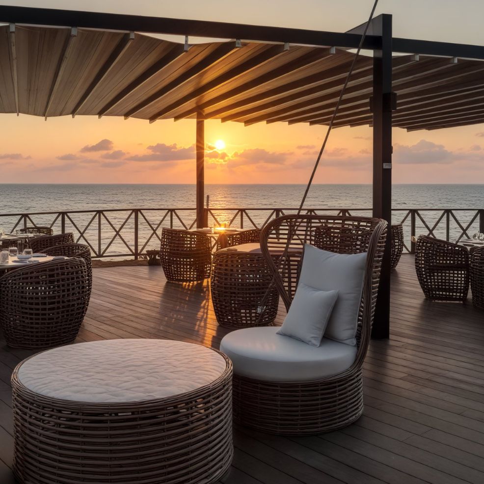 An outdoor patio adorned with wicker chairs and tables by the ocean at sunset creates a perfect setting for a destination wedding.
