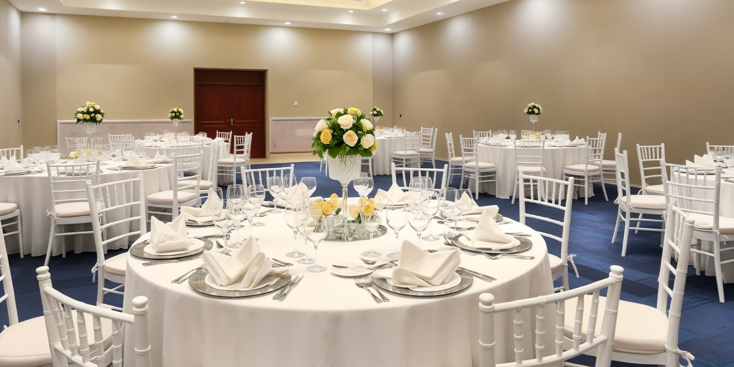 A banquet hall elegantly arranged with round tables for a destination wedding, showcasing white linens and floral centerpieces.