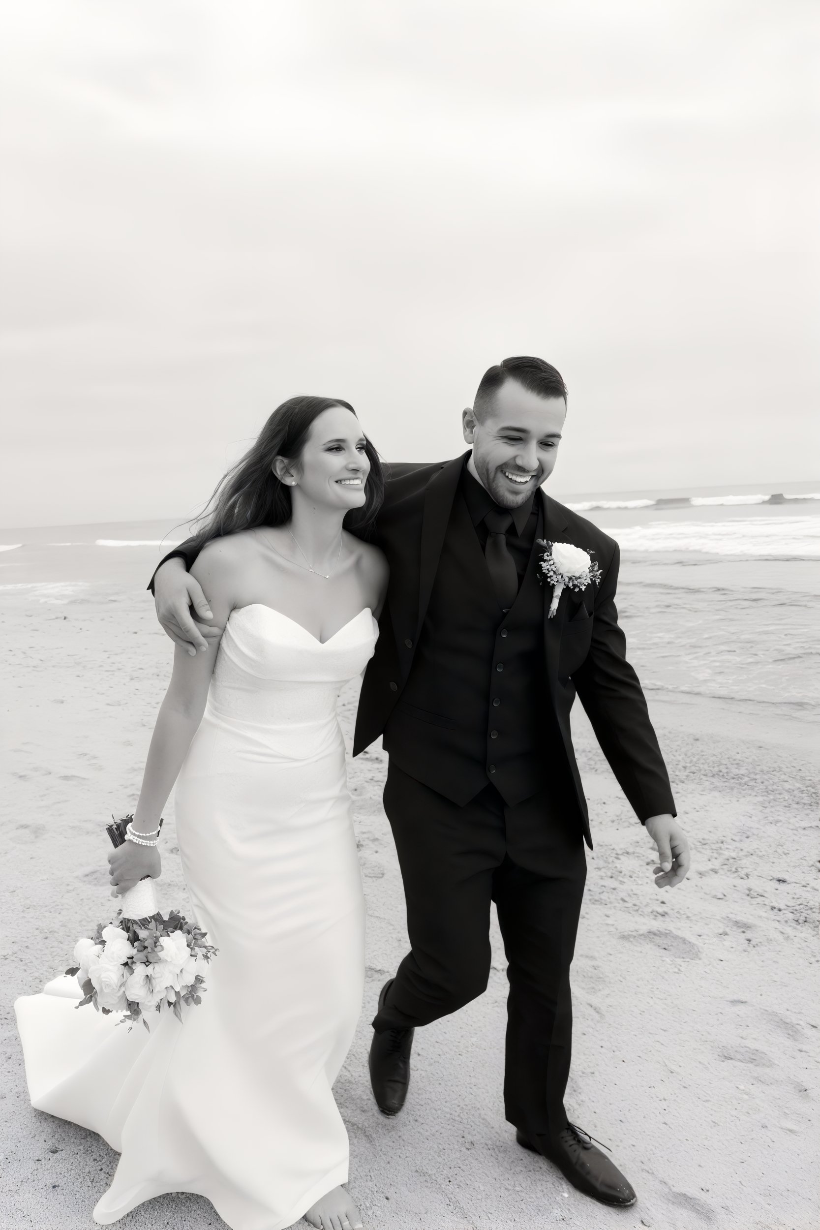 Kirsten and Angel, elegantly dressed in formal attire, are captured smiling on a picturesque beach with the ocean serving as a breathtaking backdrop for their destination wedding.