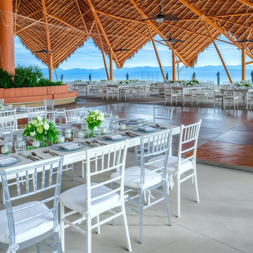 Charming outdoor dining space featuring white tables and chairs beneath a wooden roof, perfect for a destination wedding setting.