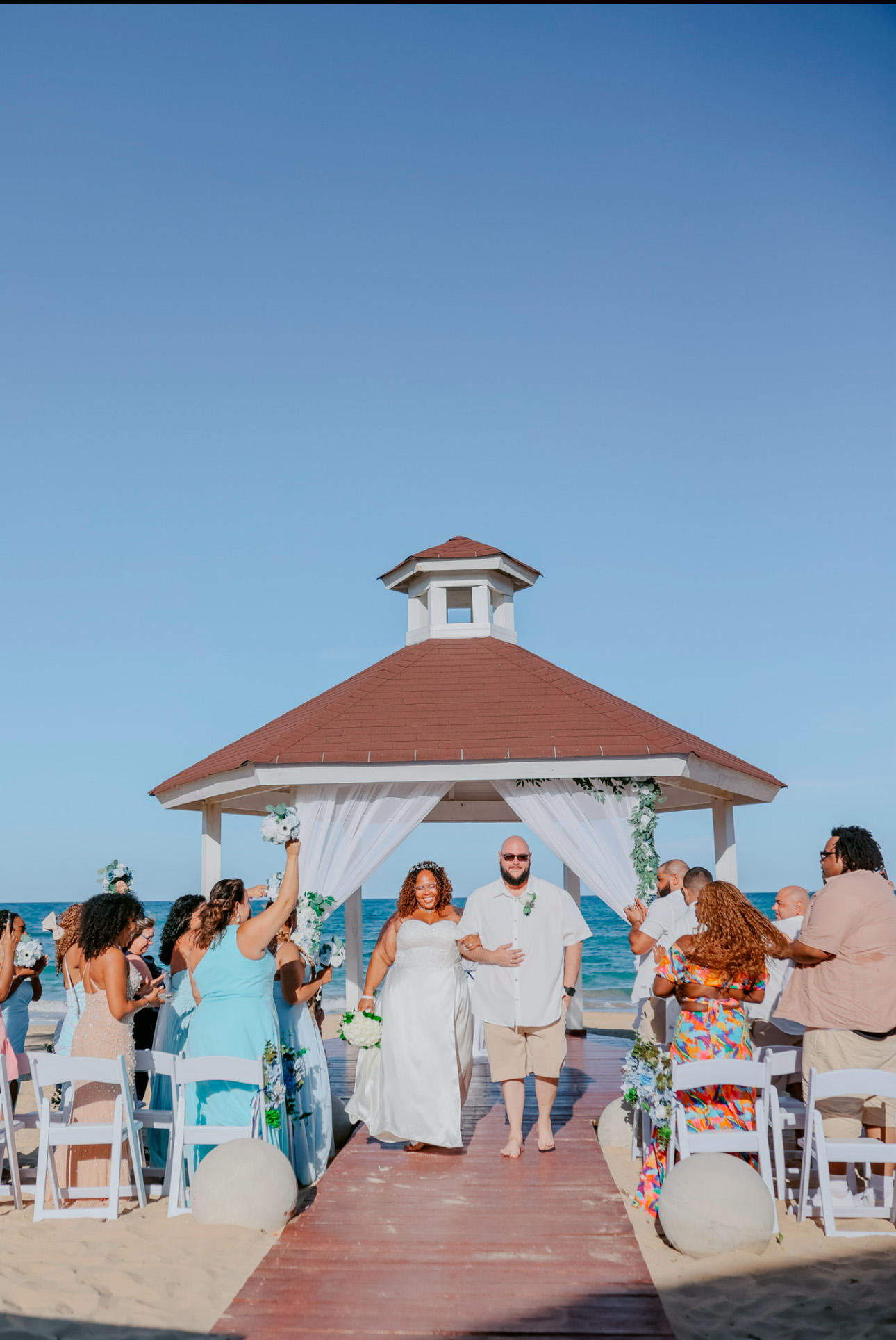 A couple strolls down the aisle at their destination wedding on the beach, exchanging vows beneath a charming gazebo.