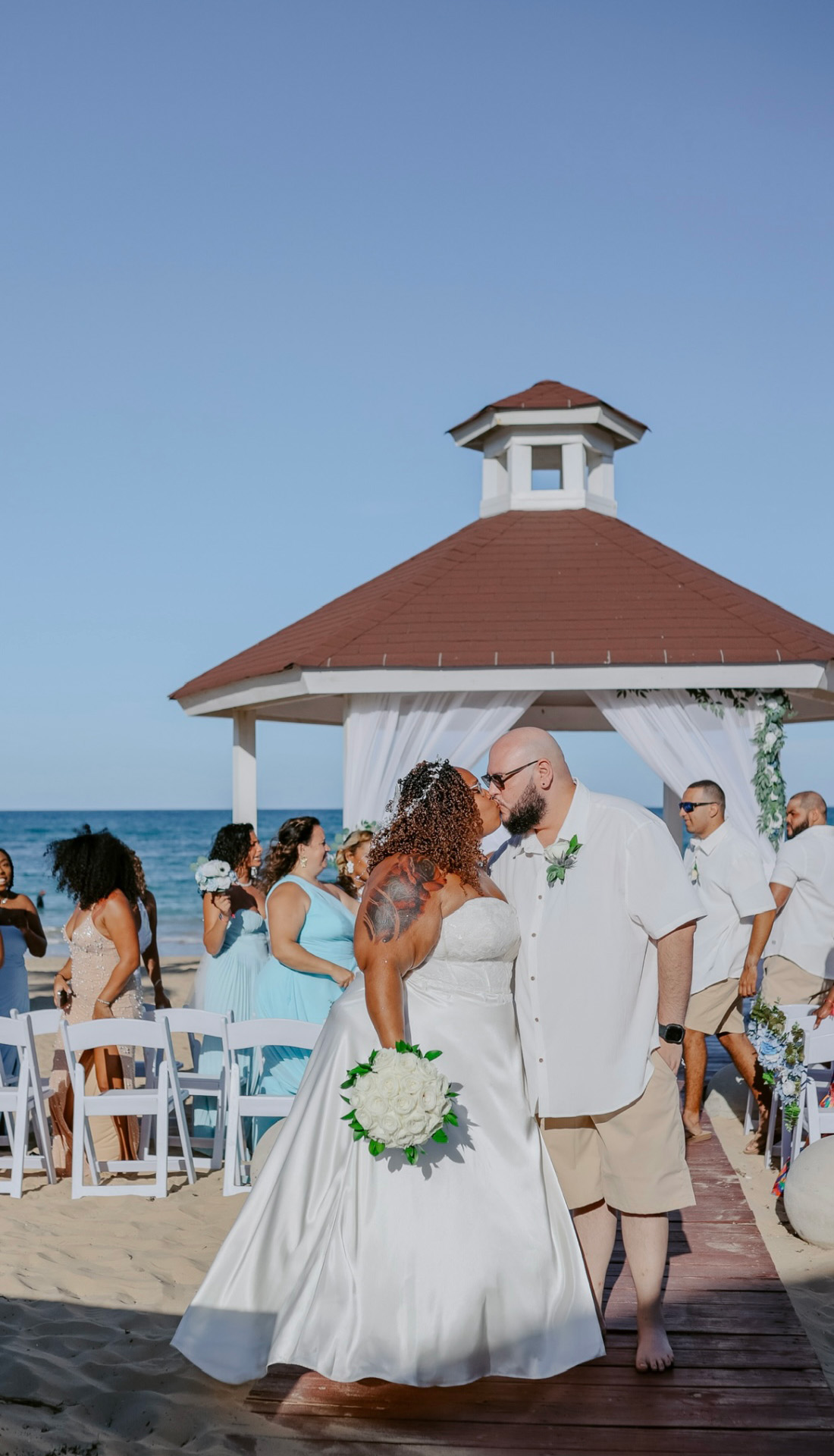The bride and groom stroll down the sandy aisle of their romantic beach destination wedding, framed by a charming gazebo.