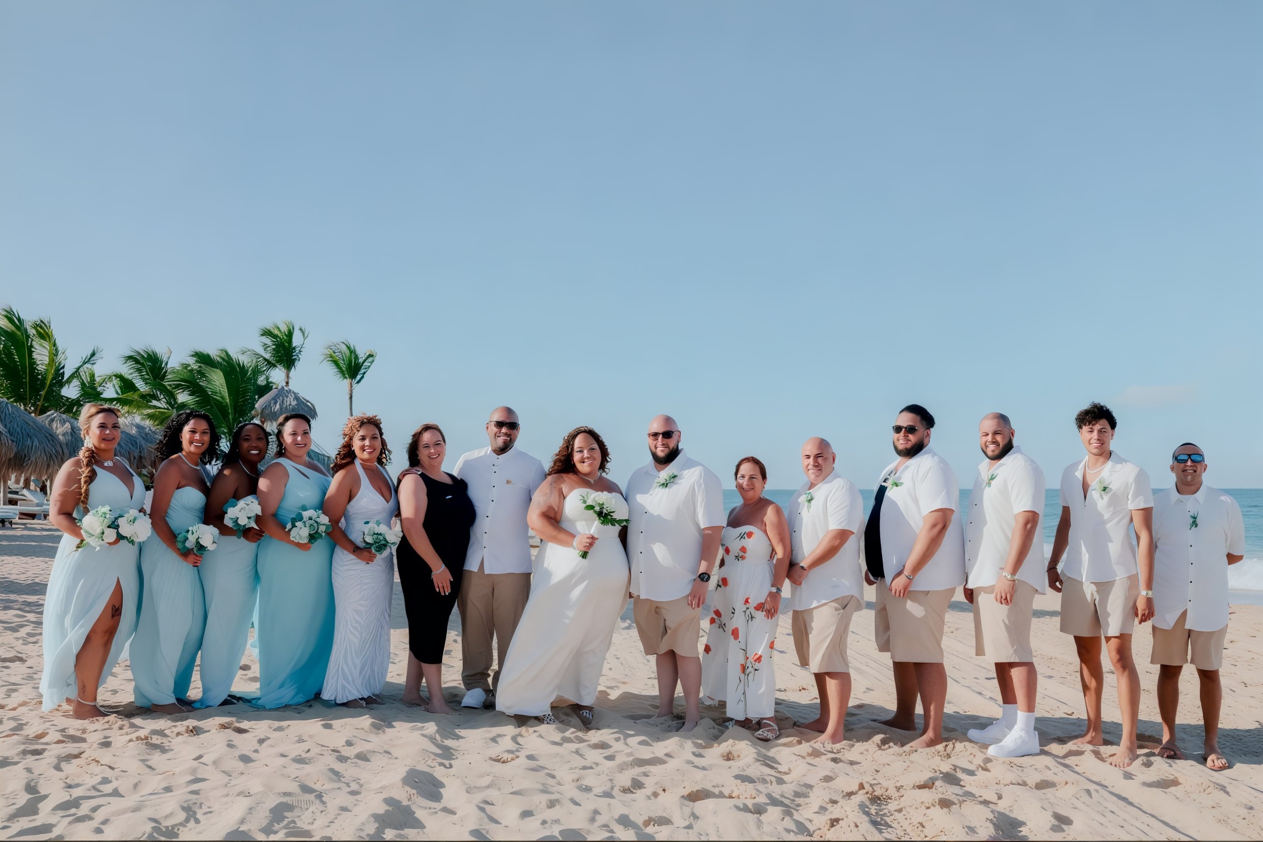 A wedding group capturing memories on a beach beneath a pristine blue sky.