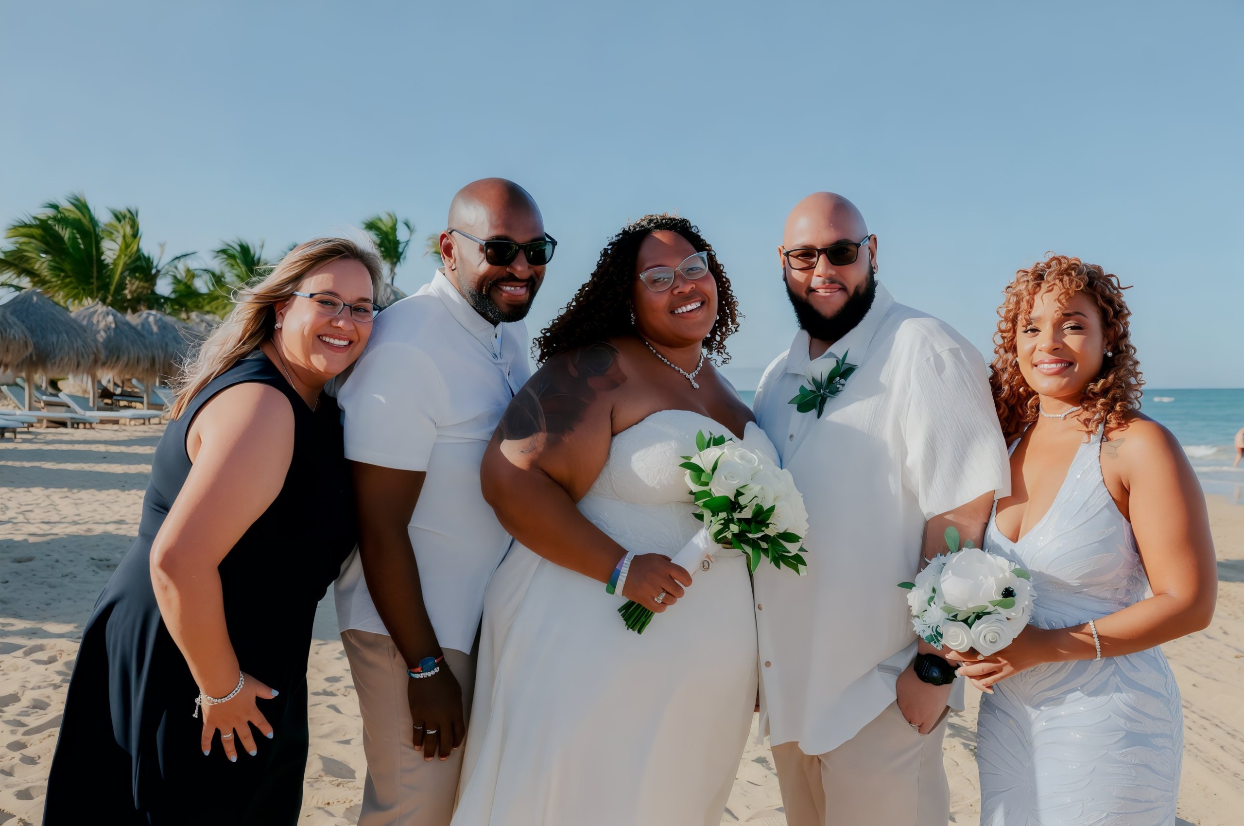 Five individuals beaming in their wedding attire on a sunny beach, capturing the joy of a destination wedding.