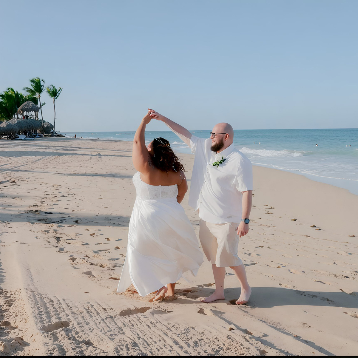 A couple, elegantly dressed in wedding attire, dances on a sandy beach, embodying the essence of a destination wedding.