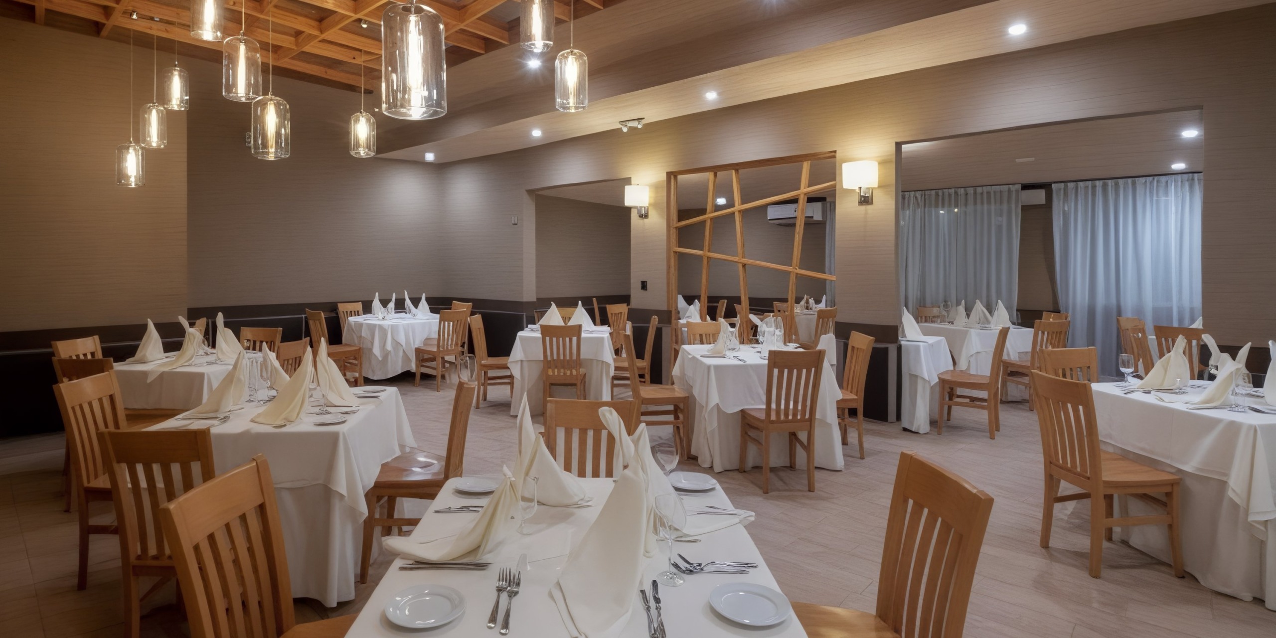 A vacant restaurant dining area elegantly arranged for a destination wedding, featuring wooden chairs and tables adorned with crisp white tablecloths and napkins.