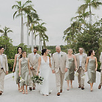 The bridal party, dressed in elegant beige and green, leisurely strolls through the lush outdoors beneath towering palm trees at this picturesque destination wedding.