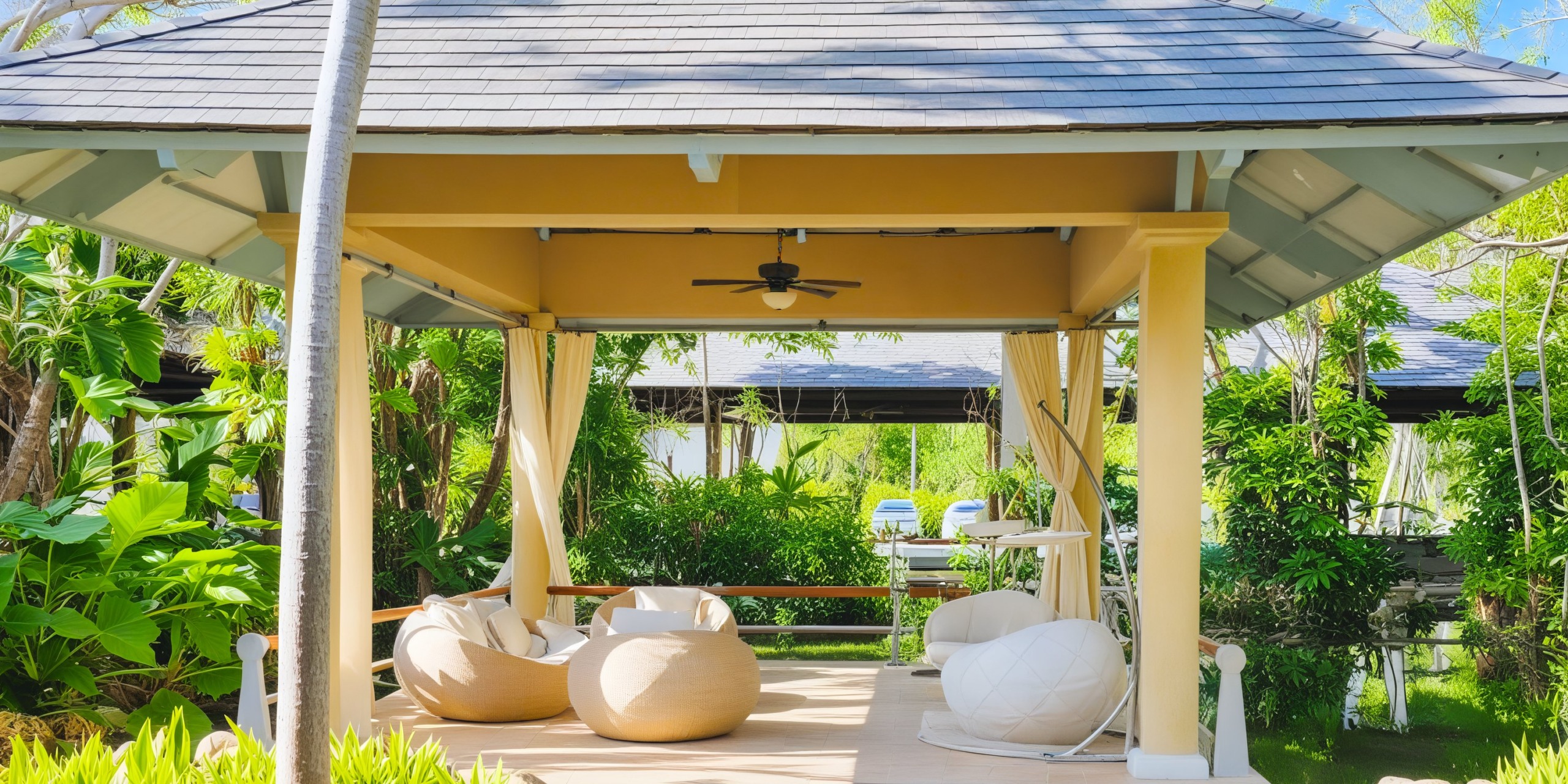A picturesque destination wedding setup featuring an outdoor gazebo adorned with lush greenery and comfortable bean bag chairs, all nestled in a sunlit garden setting.