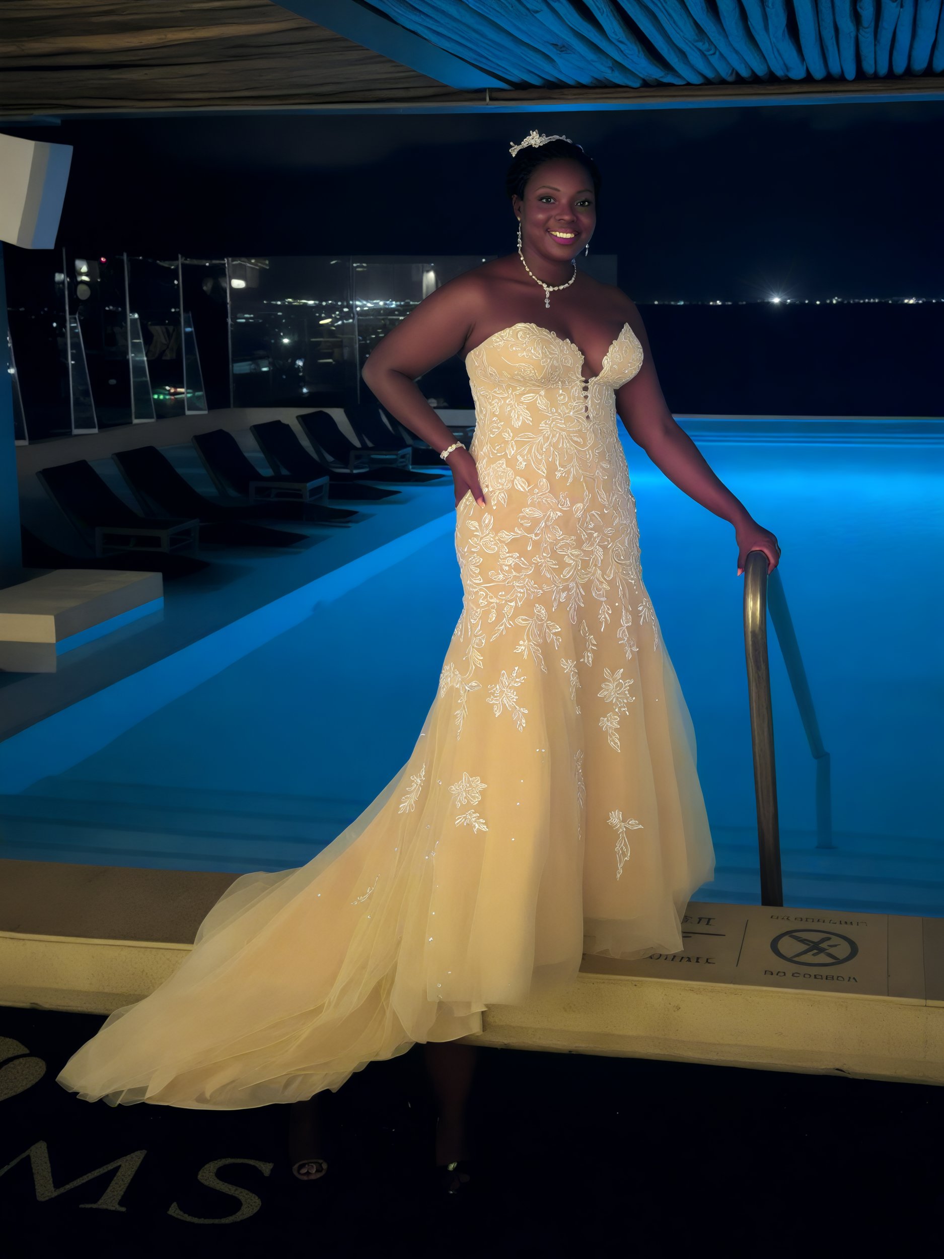 Draped in a stunning Sheneka and Andre gown, a woman elegantly poses by the illuminated pool under the night sky, capturing the essence of a dream destination wedding.
