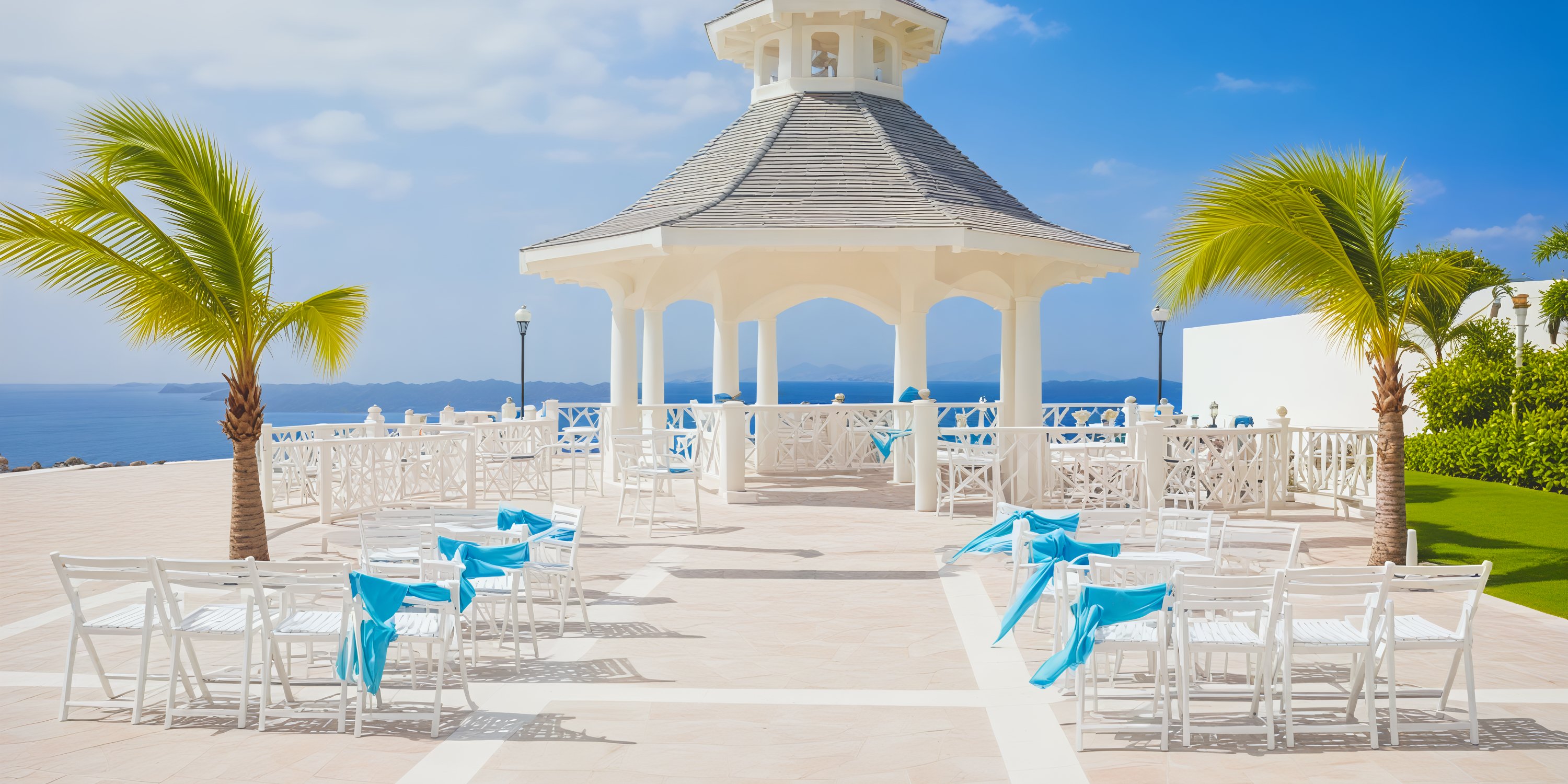 A white gazebo adorned with chairs draped in blue sashes, offering a stunning view of the ocean beneath a clear sky, creates the perfect setting for a destination wedding.