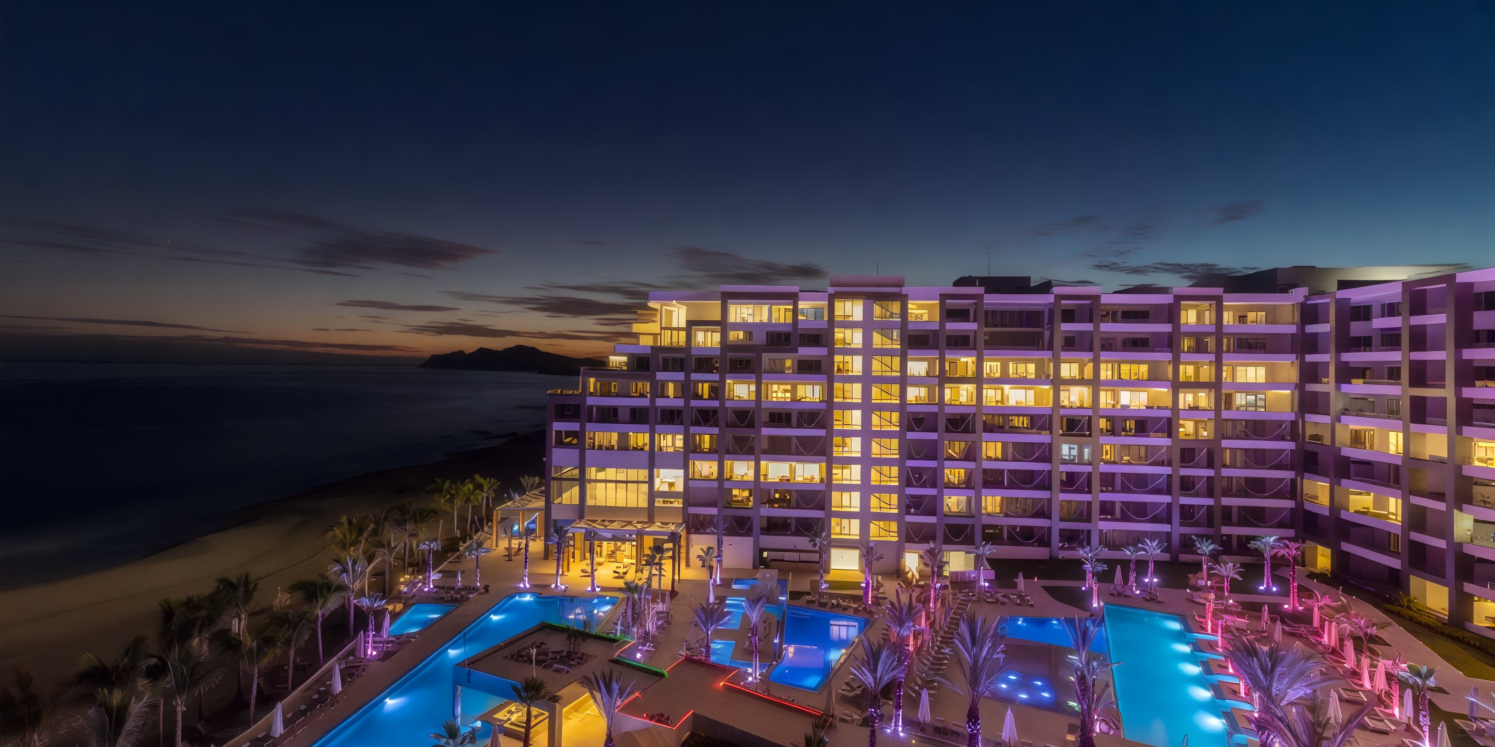 The Garza Blanca Los Cabos hotel and pool are illuminated at night by the beach in vibrant shades of purple and blue, creating a breathtaking setting for a destination wedding.