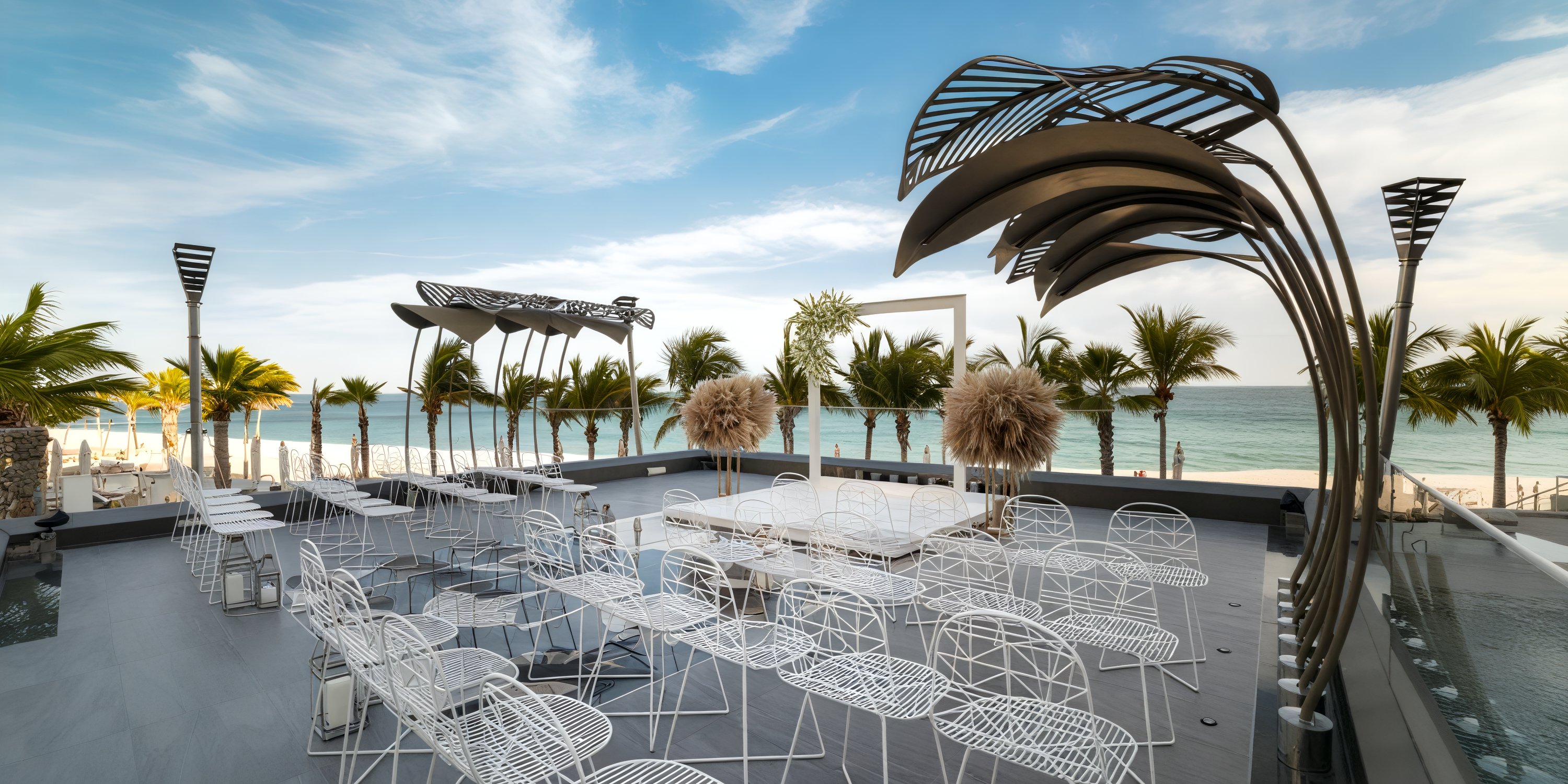 Garza Blanca Los Cabos: A stunning beachfront destination wedding venue featuring white chairs, palm sculptures, and a clear sky.