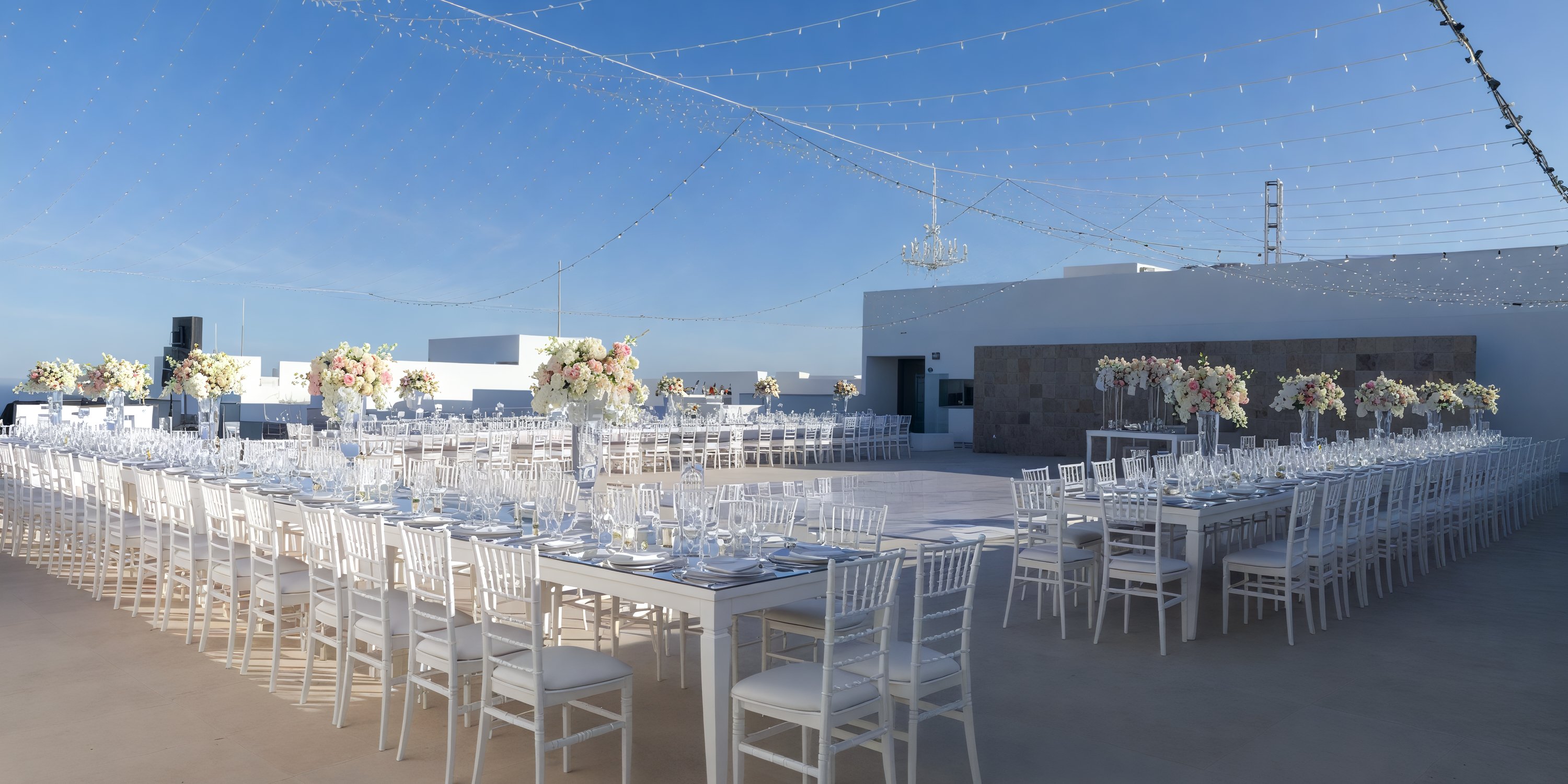 Experience a breathtaking destination wedding at Garza Blanca Los Cabos, featuring elegant white tables and chairs adorned with beautiful florals, all set under enchanting string lights.