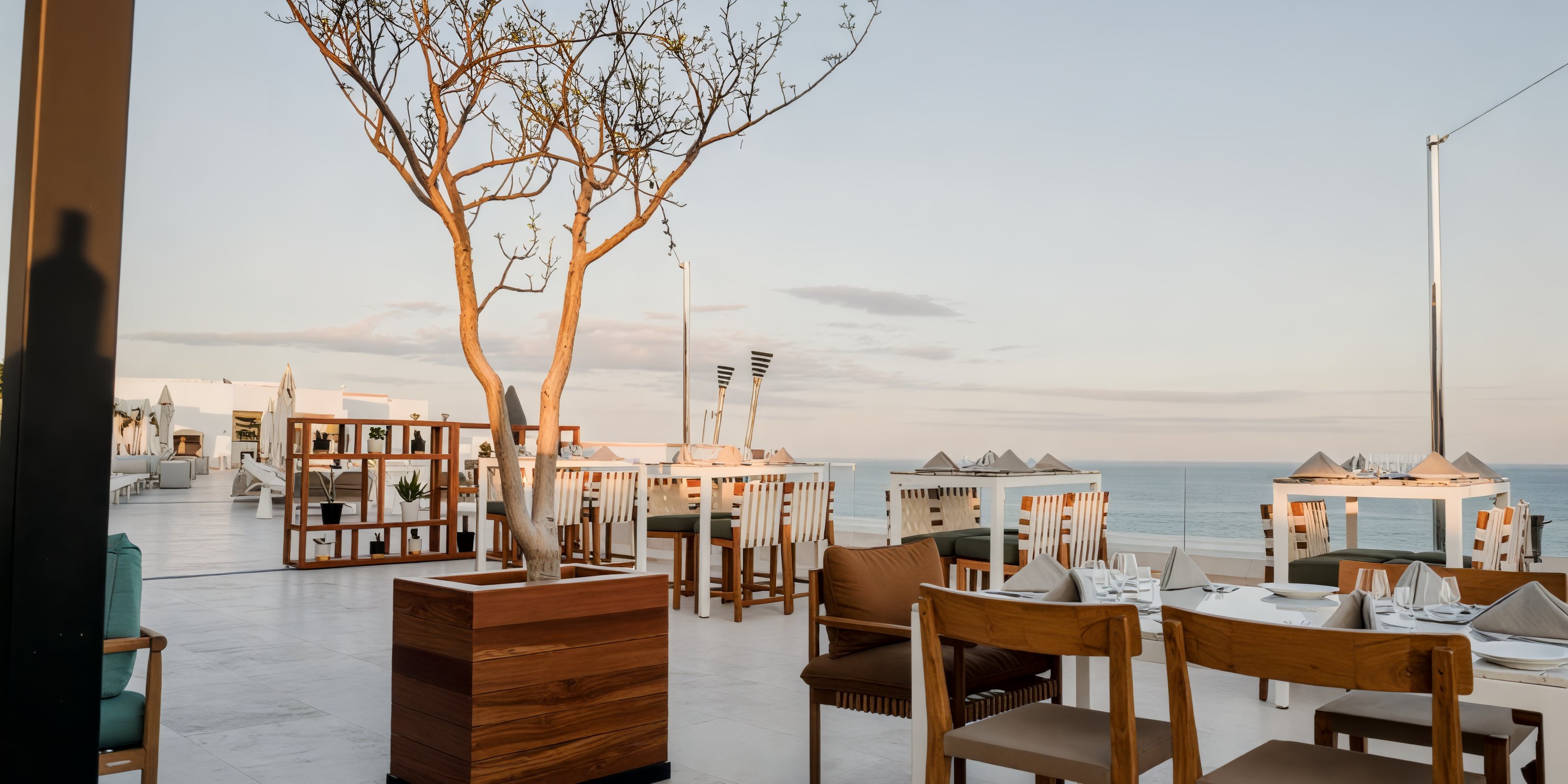 An outdoor restaurant at Garza Blanca Los Cabos, featuring tables, chairs, and a decorative tree, provides a picturesque setting ideal for a destination wedding.
