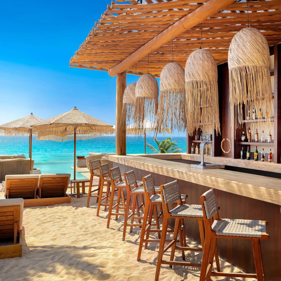 A beachside bar perfect for a destination wedding, featuring wooden stools, charming thatched pendant lights, and stunning ocean views.