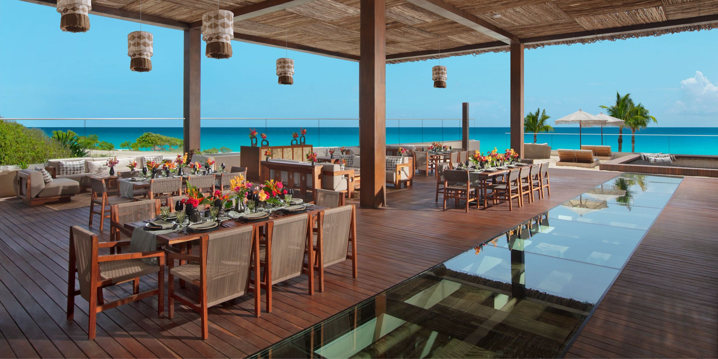 A stunning outdoor dining area perfect for a destination wedding, featuring wooden furniture and floral centerpieces. Enjoy breathtaking ocean views along with a picturesque pool walkway.