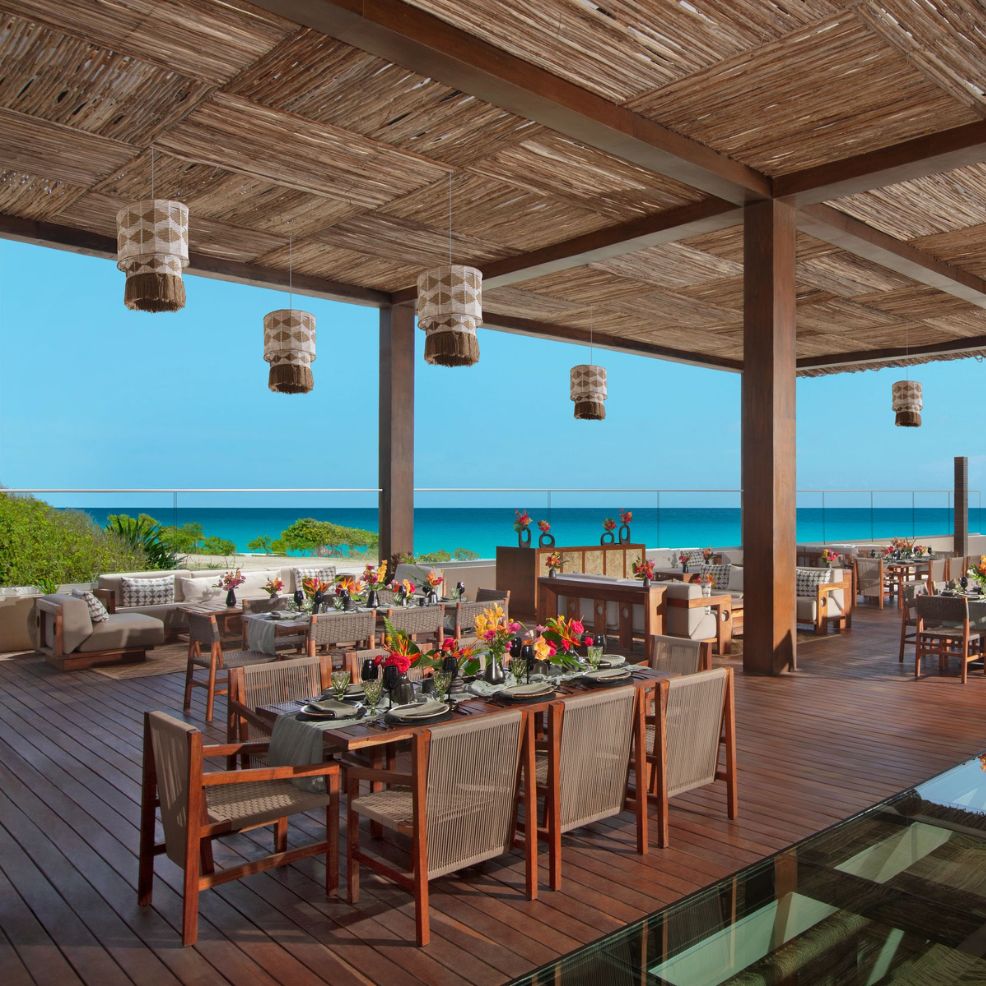 An outdoor dining area perfect for a destination wedding, featuring ocean views, wooden furniture, and colorful table settings.