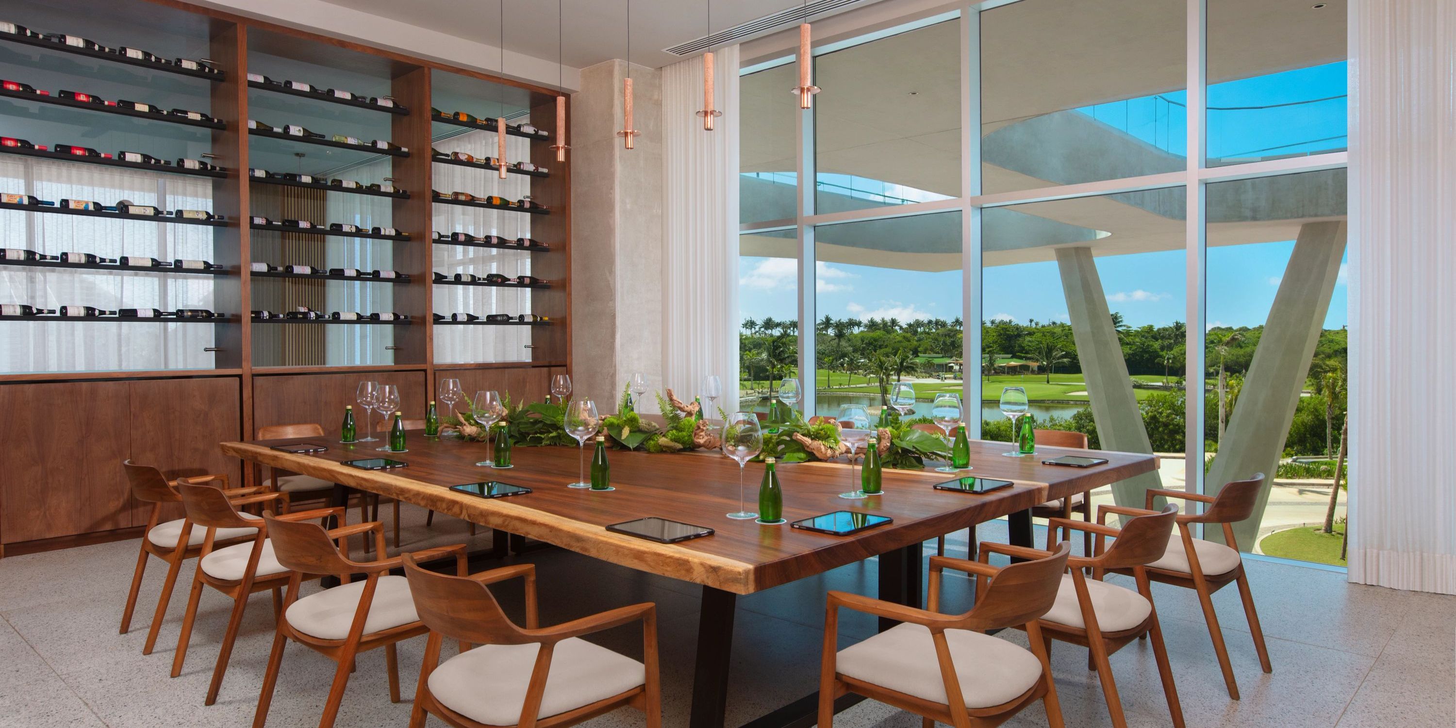 An elegant dining room designed for a destination wedding, featuring a large wooden table surrounded by chairs and an exquisite wine display.