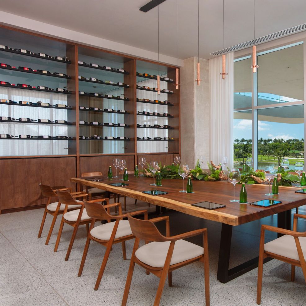 A dining room perfect for a destination wedding, featuring a wooden table, elegant chairs, a wine rack, and large windows that let natural light illuminate the space.
