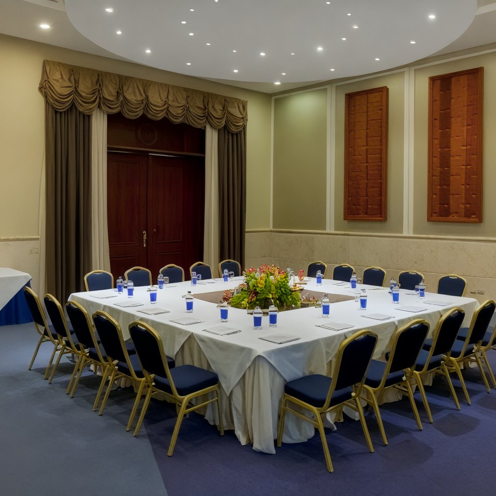 A U-shaped conference table setup, adorned with water glasses and a floral centerpiece, is elegantly prepared in the meeting room, offering inspiration for an intimate destination wedding reception.