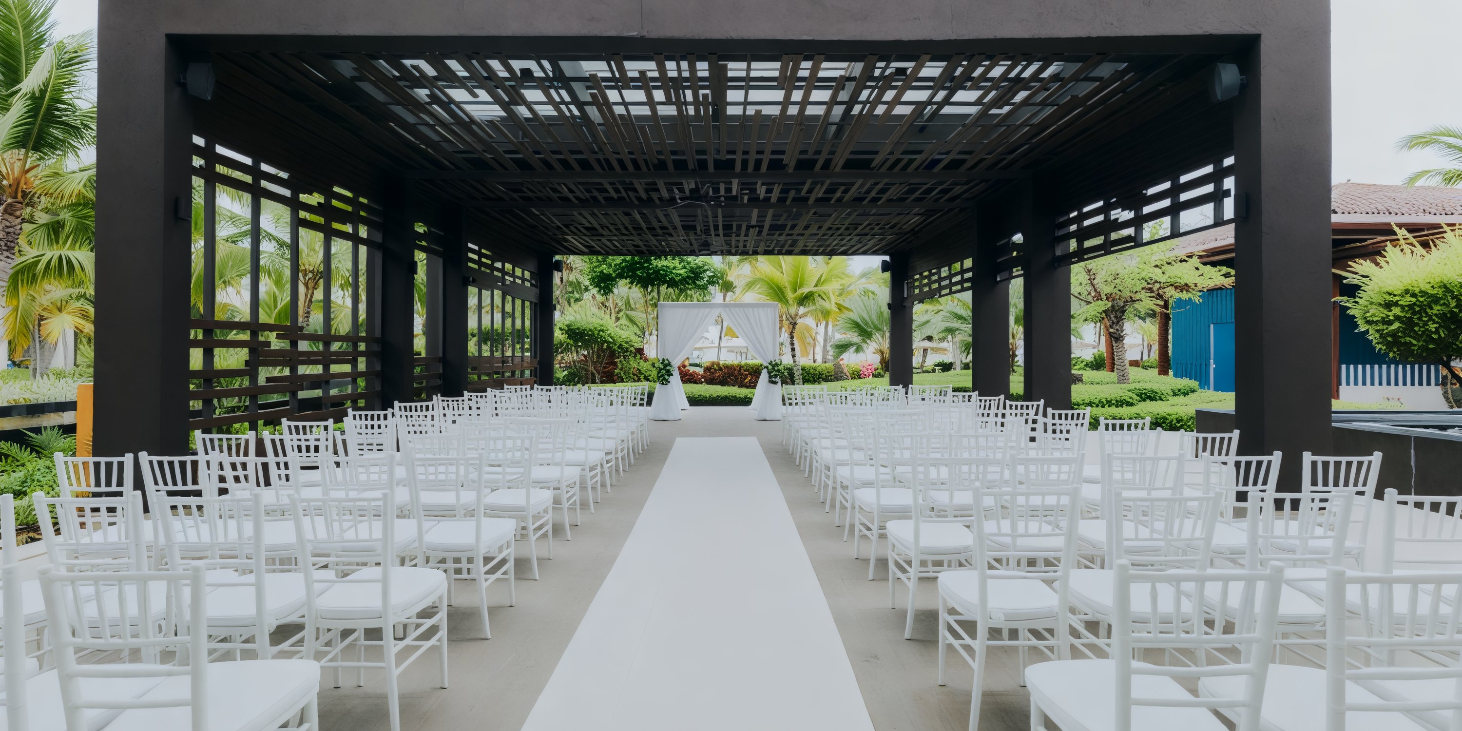 A stunning destination wedding venue featuring a modern pergola, complete with white chairs arranged along a central aisle.