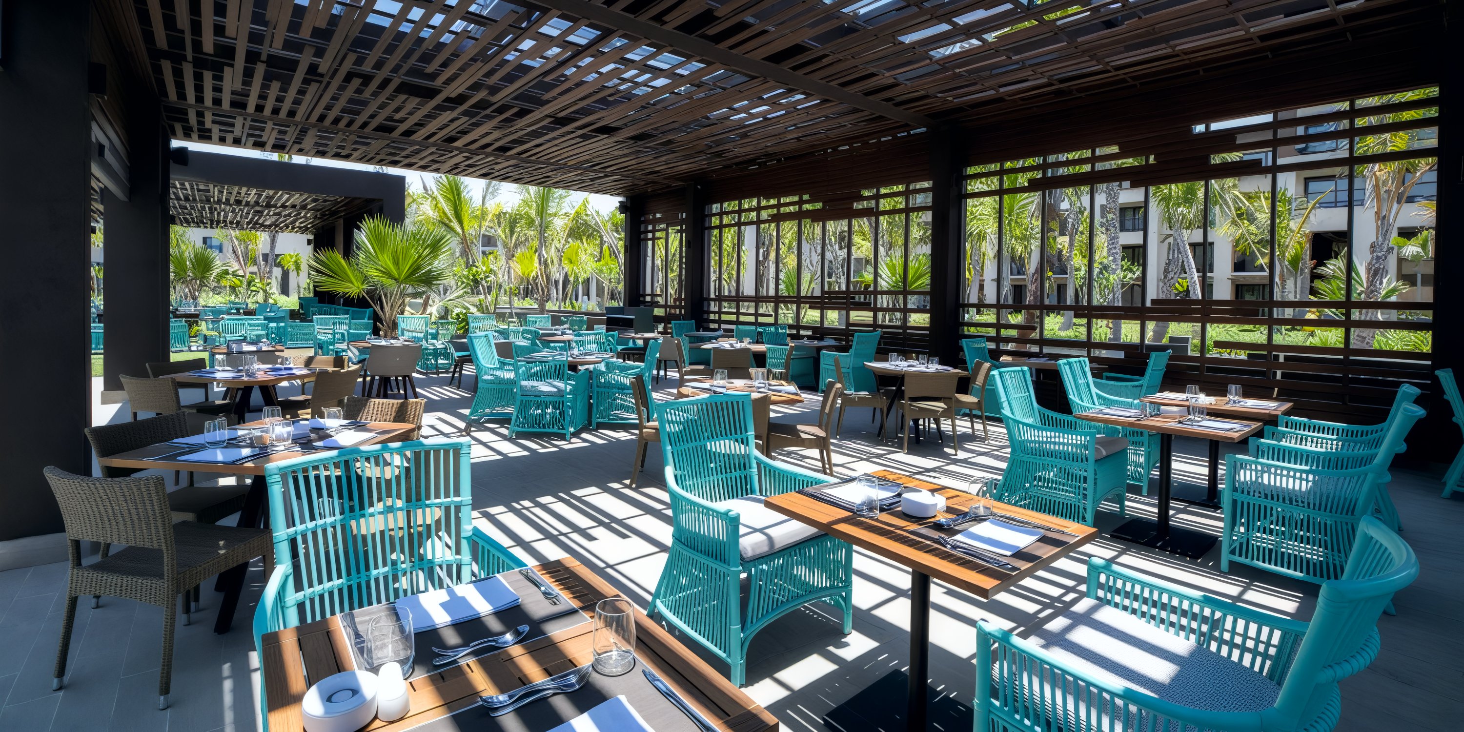 Experience a destination wedding setting featuring outdoor restaurant seating with turquoise chairs, wooden tables, and captivating plant views.