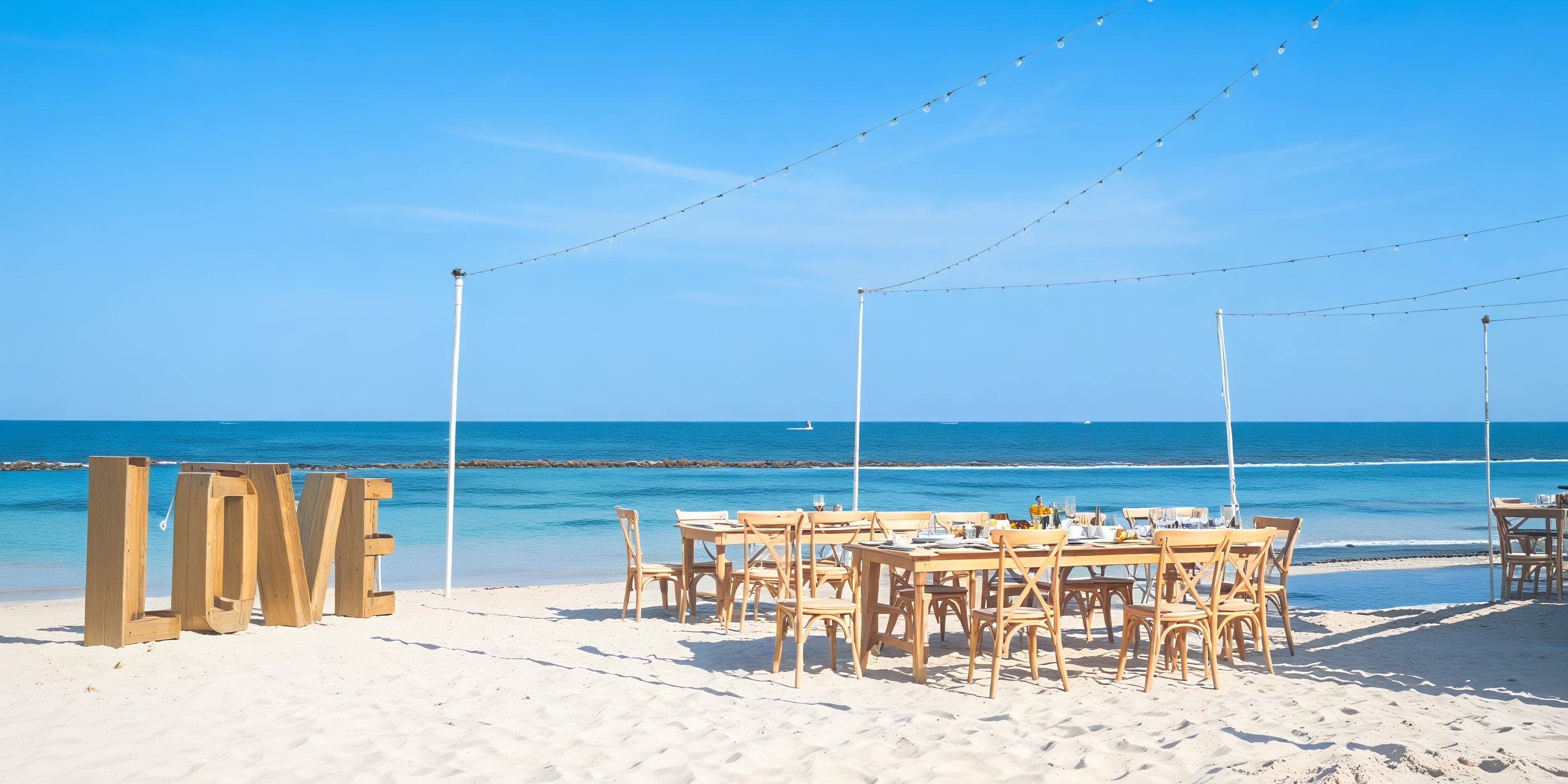 For a dreamy destination wedding, imagine a beachside scene complete with elegantly arranged tables and chairs, enchanting string lights casting a warm glow, and a grand "LOVE" sign set in the sand.