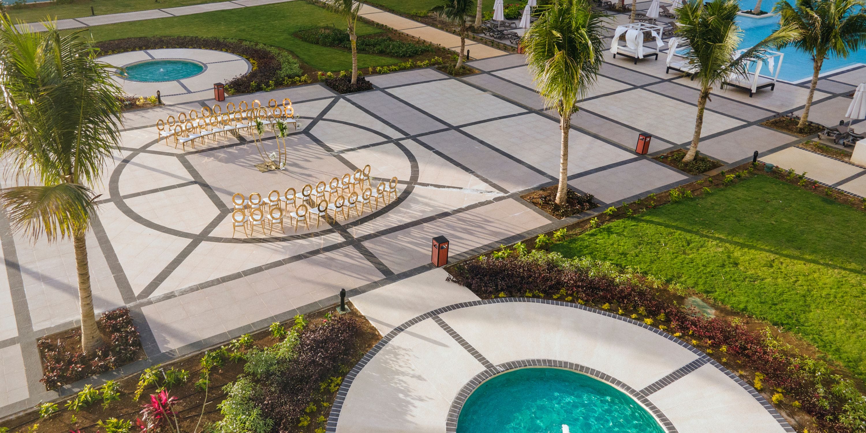 Aerial view of a courtyard set for a destination wedding with circular pools, chairs, palms, and lawns.