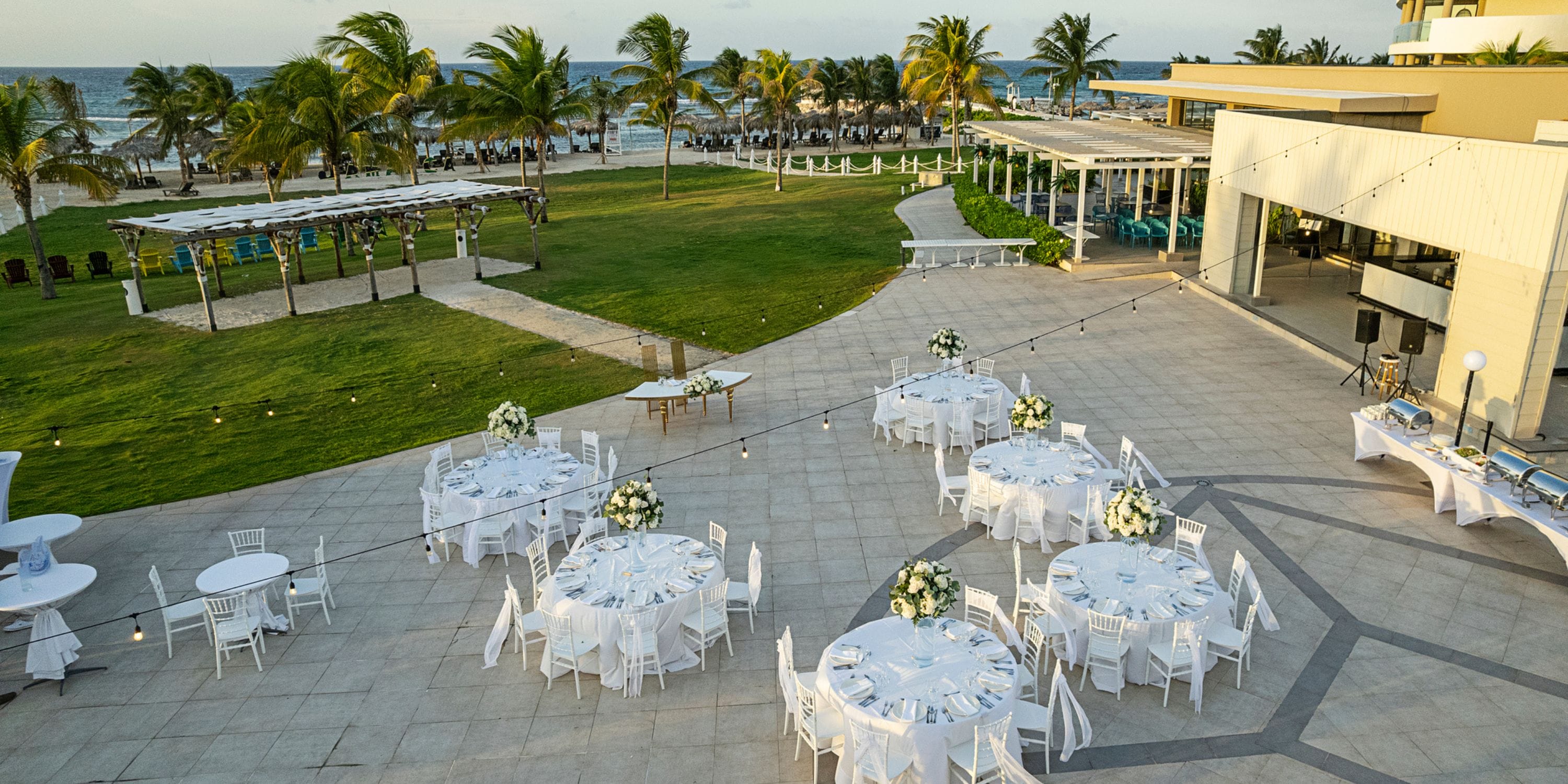 Destination wedding reception featuring round tables and chairs arranged outdoors by a beachside resort.