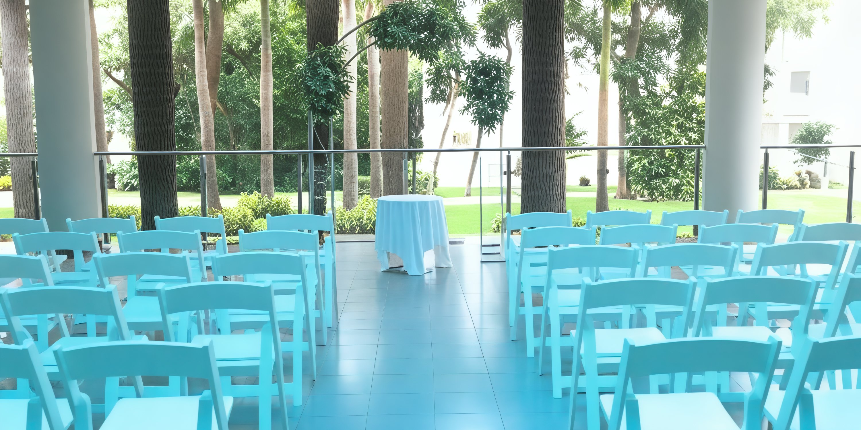 A serene destination wedding scene features turquoise chairs and a petite table nestled beneath the trees.