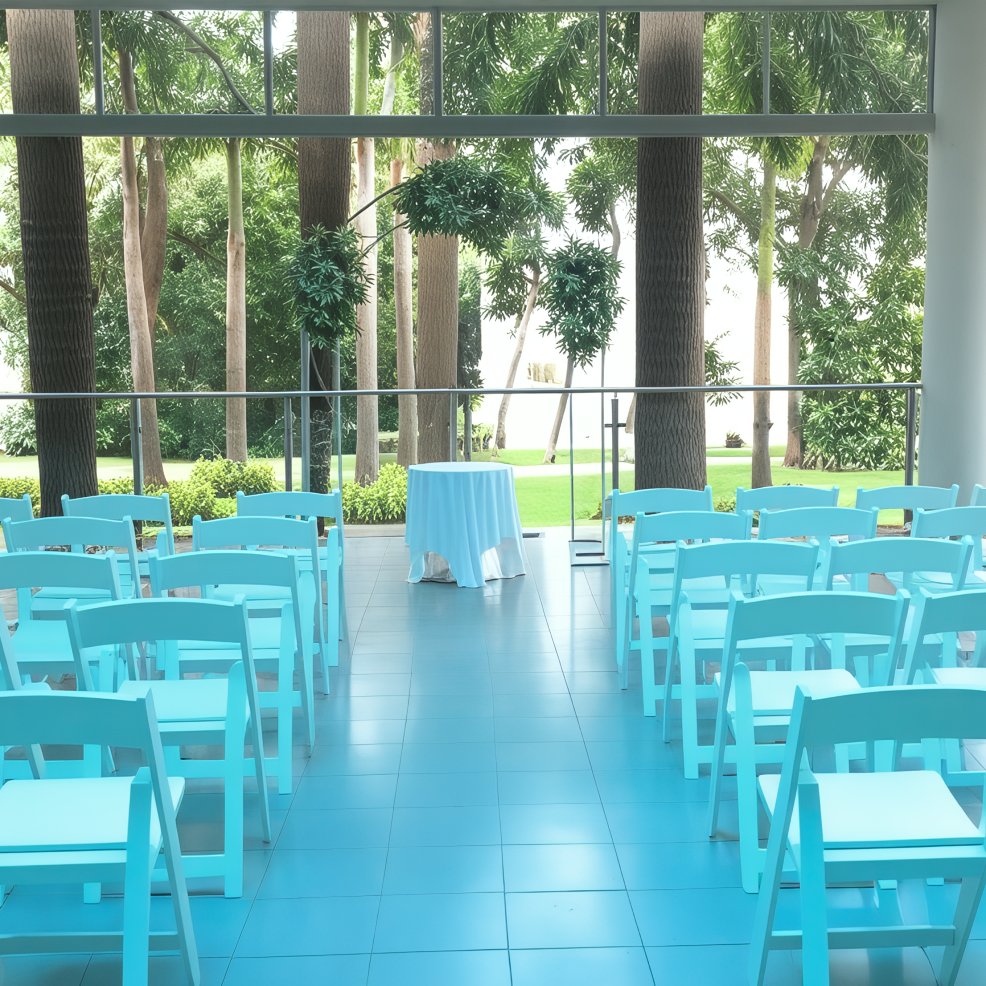 A picturesque outdoor wedding ceremony setup features mint green chairs arranged to face a small table, beautifully nestled amidst a grove of trees.