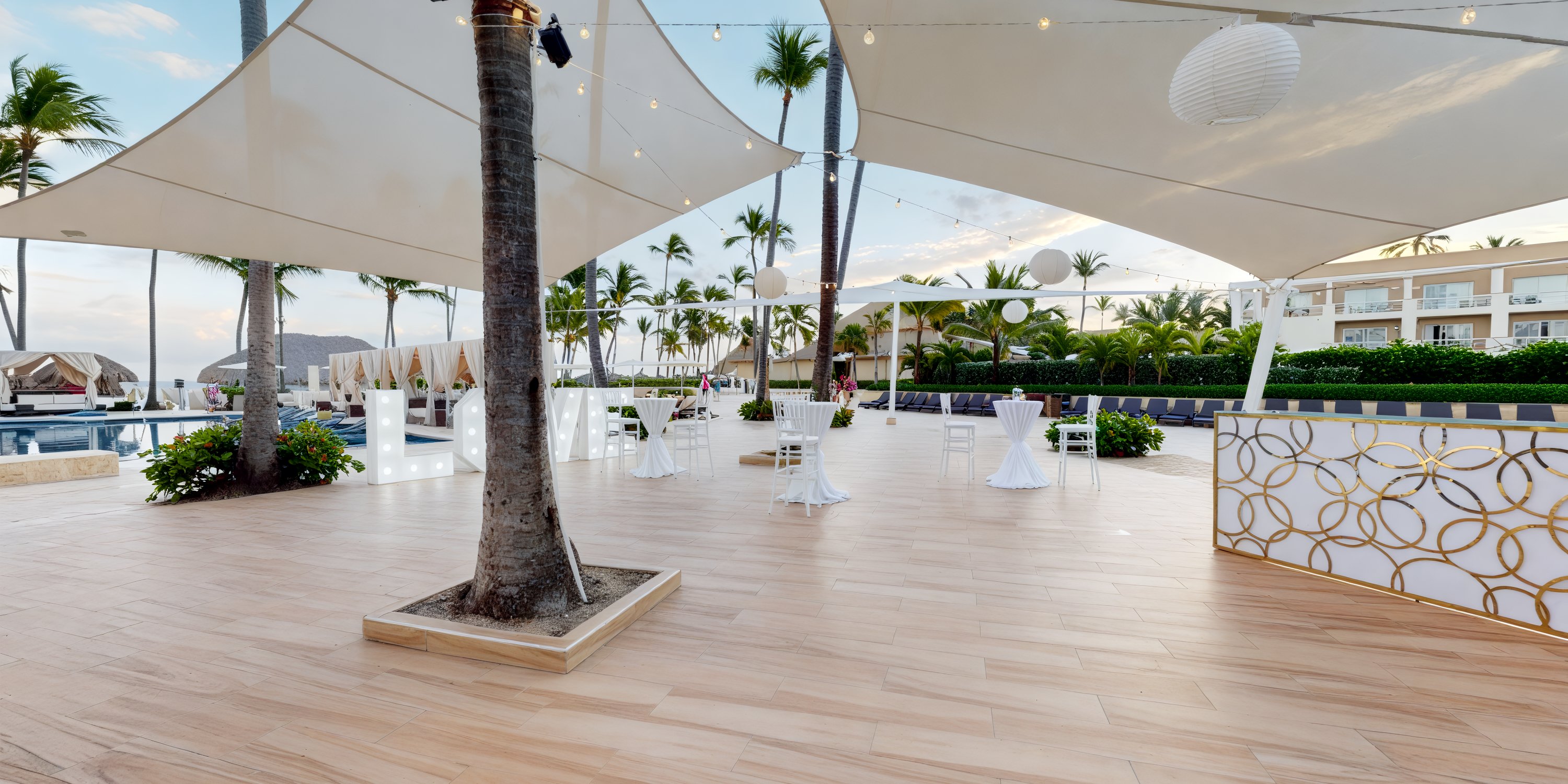 An outdoor wedding venue featuring a white canopy, elegantly arranged tables, and a lush tropical setting. Ideal for a destination wedding.