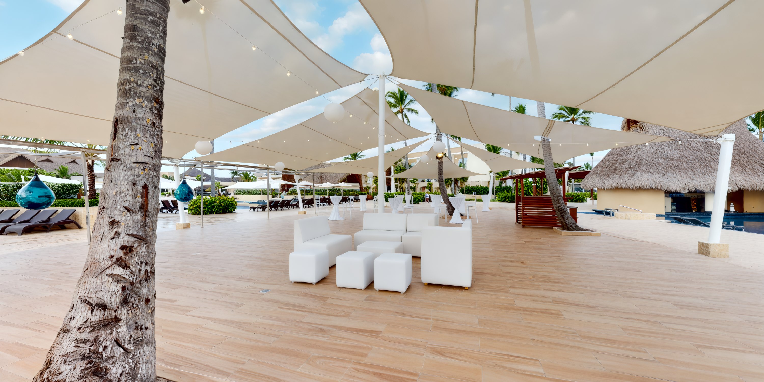 A charming outdoor seating area featuring white couches under a canopy, nestled amid palm trees, perfect for a destination wedding.